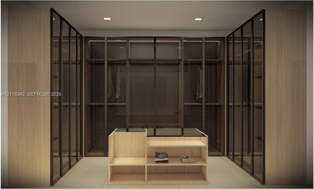 Custom dressing area featuring floor-to-ceiling cabinetry with glass-panel doors, integrated shelving, and a central built-in island with a countertop surface