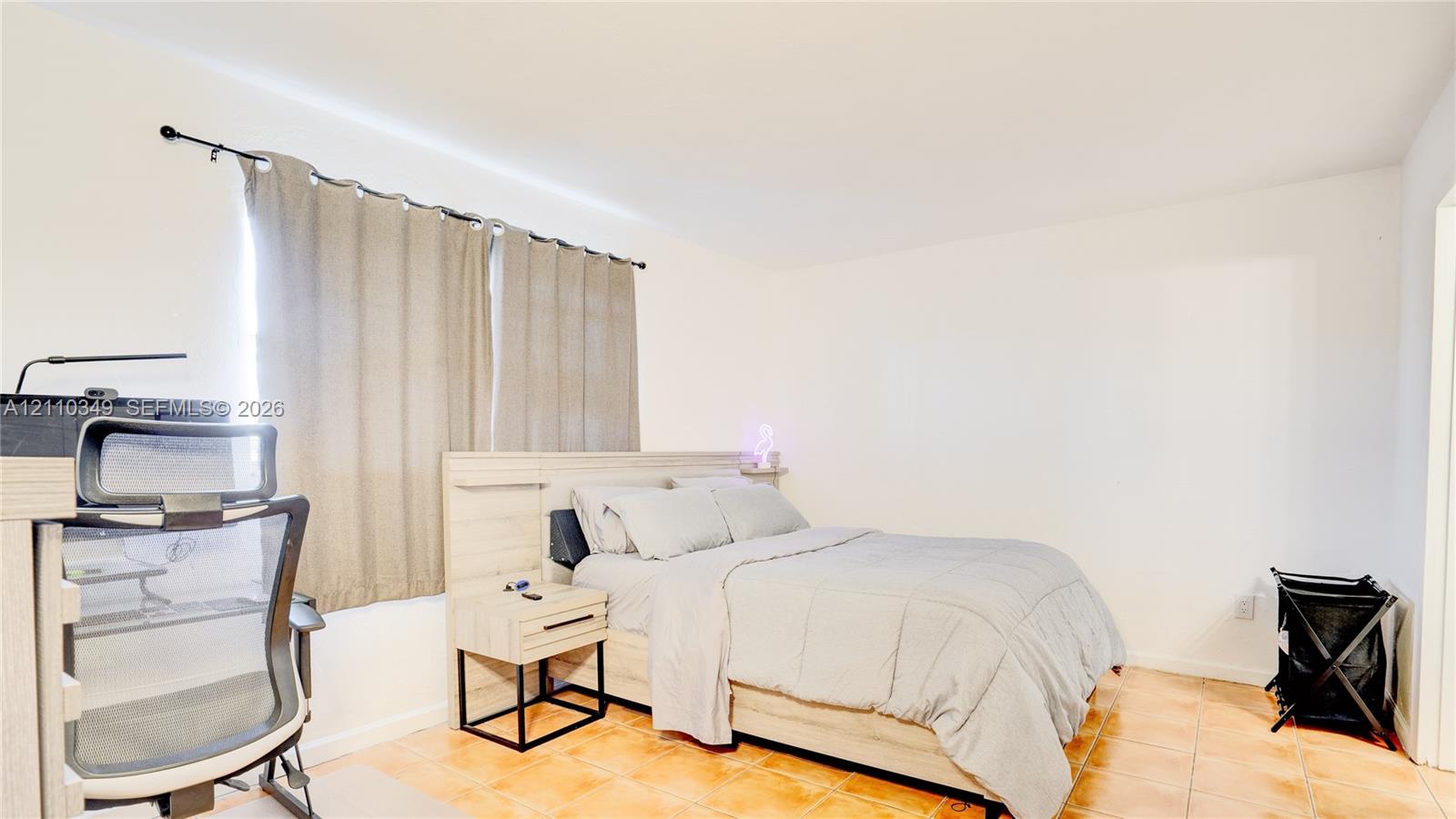 Neutral-toned interior space featuring light-colored tile flooring, smooth white walls, and a window with a mounted curtain rod
