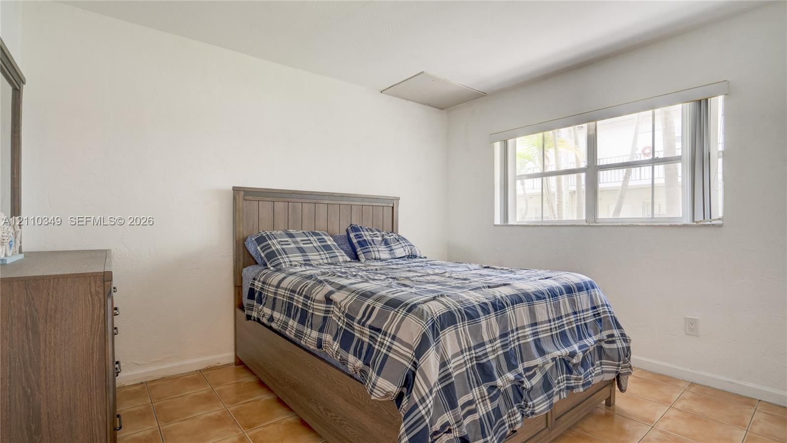 Neutral-toned bedroom featuring ceramic tile flooring, smooth wall finishes, and a window with horizontal blinds