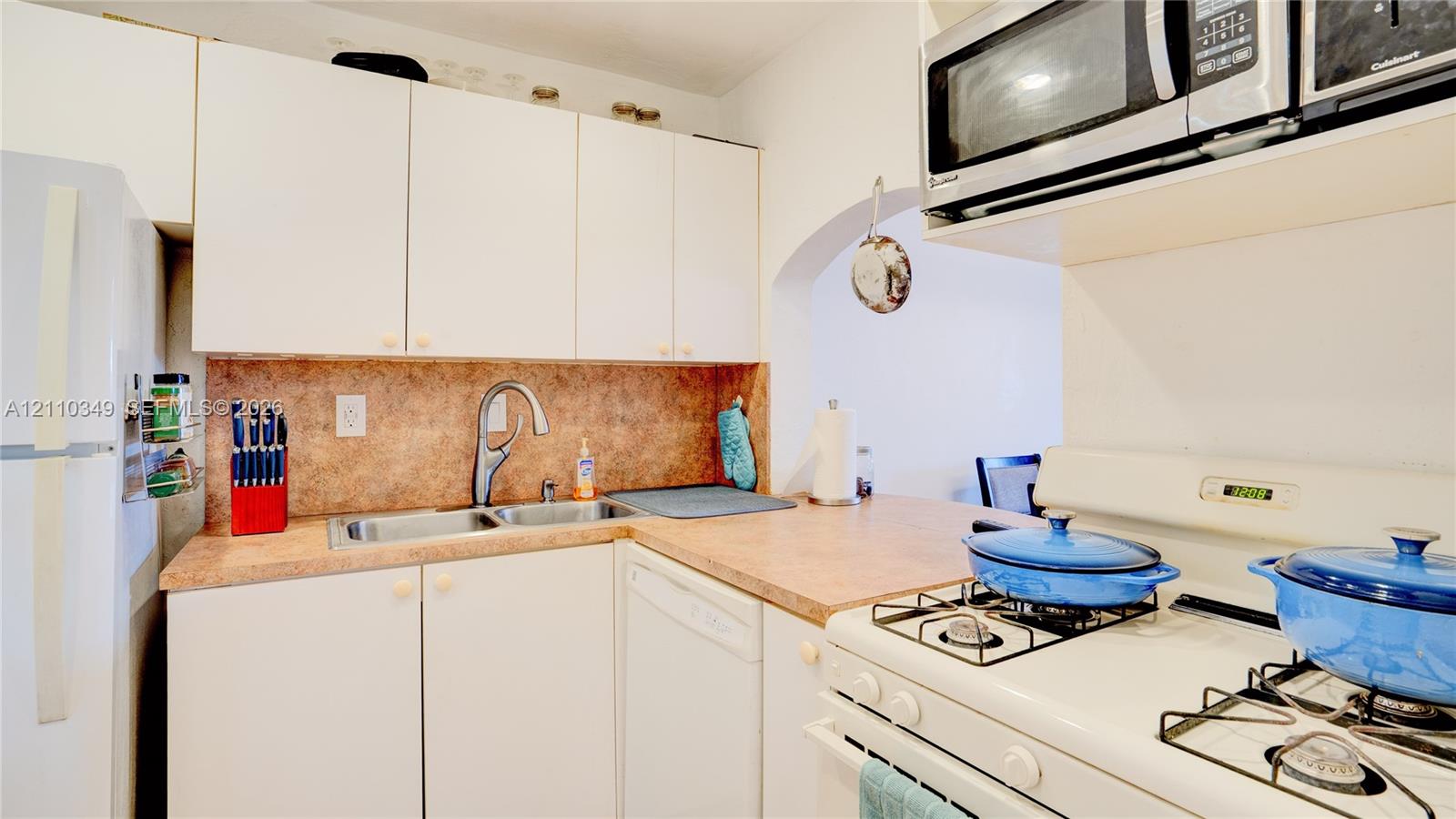 Kitchen featuring white cabinetry, solid-surface countertops, dual-basin stainless steel sink with high-arch faucet, built-in stainless steel microwave, and gas range