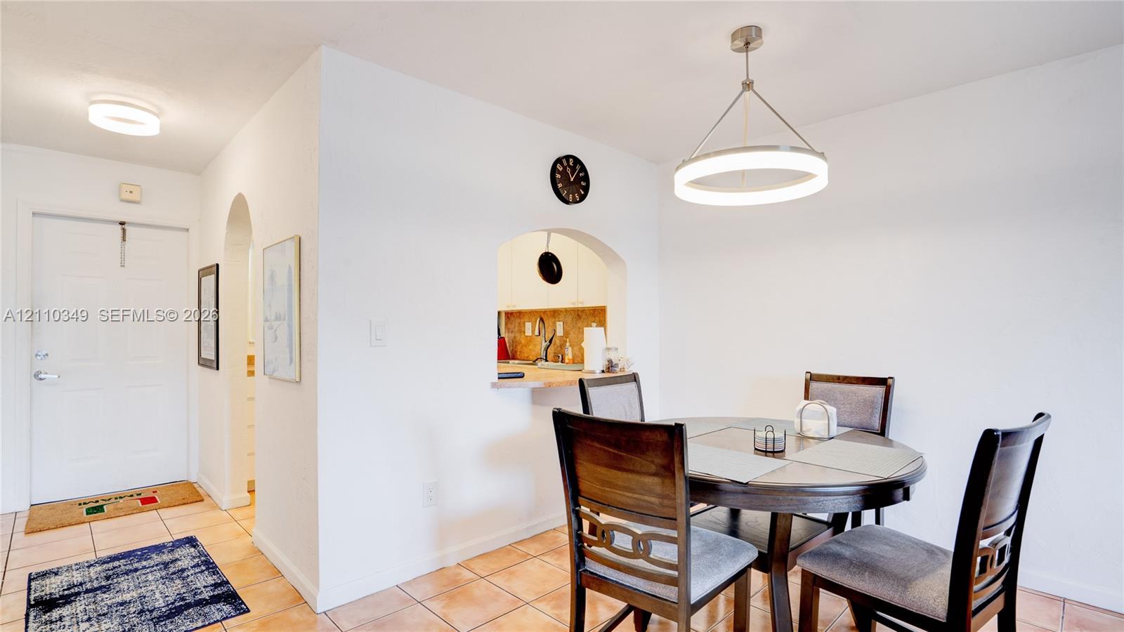 Ceramic tile flooring, arched wall pass-through, modern circular pendant lighting, and flush-mount ceiling lighting