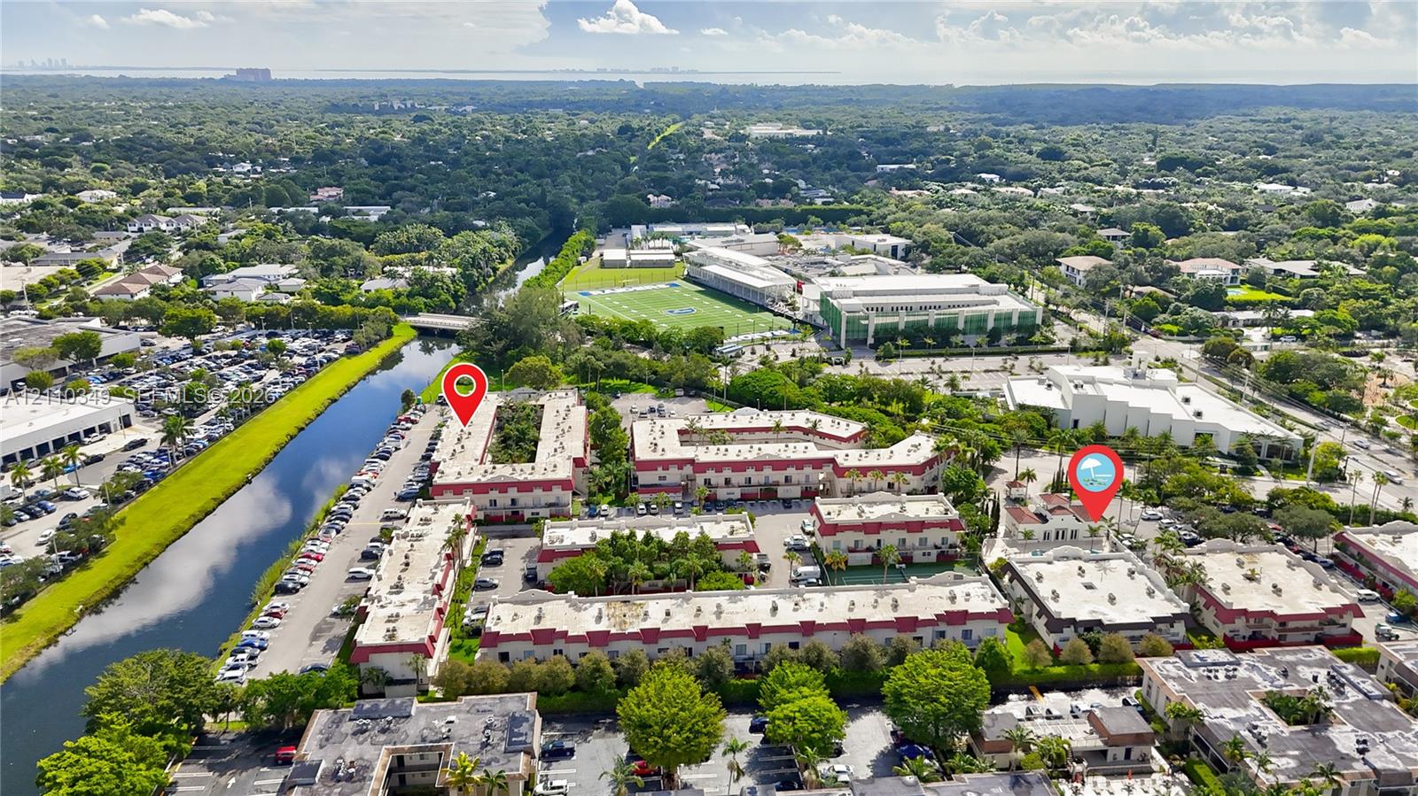 Aerial perspective of a multi-building residential complex featuring white stucco facades, terra cotta roof accents, mature landscaping, and an adjacent canal