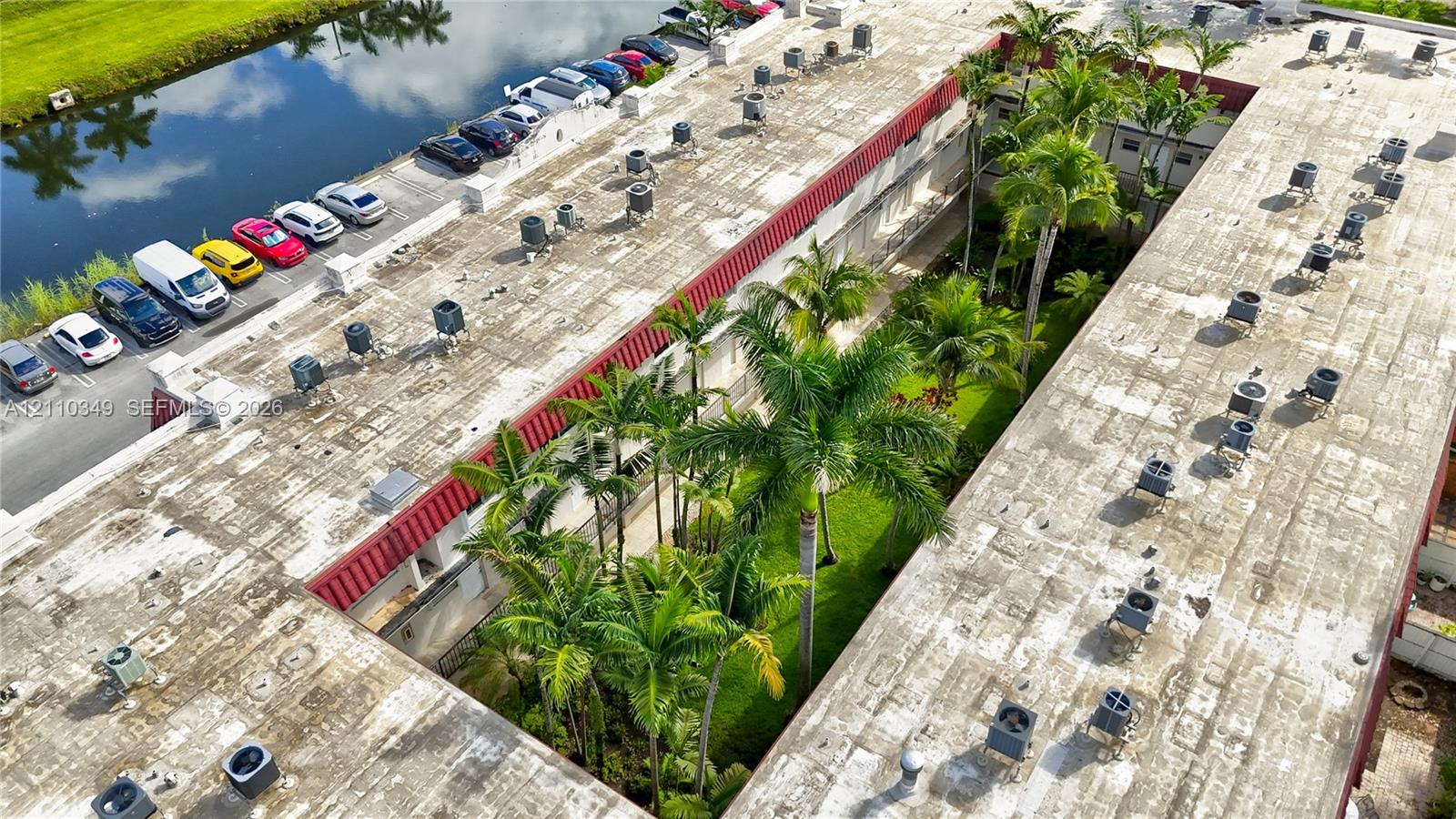 Aerial view featuring a multi-unit property with a central landscaped courtyard, mature palm trees, designated surface parking, and waterfront proximity