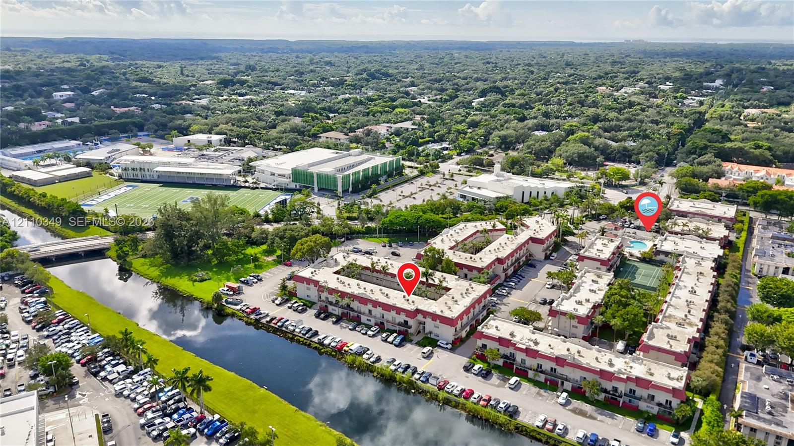 Aerial perspective of the complex featuring a multi-story building, an on-site swimming pool, and a tennis court
