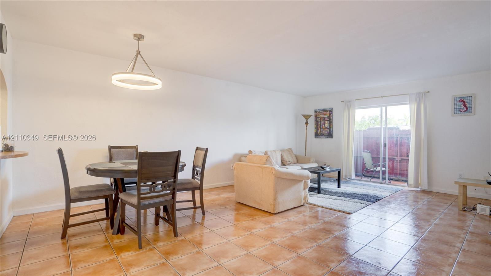 Ceramic tile flooring, minimalist circular pendant light fixture, and large glass sliding door providing outdoor access