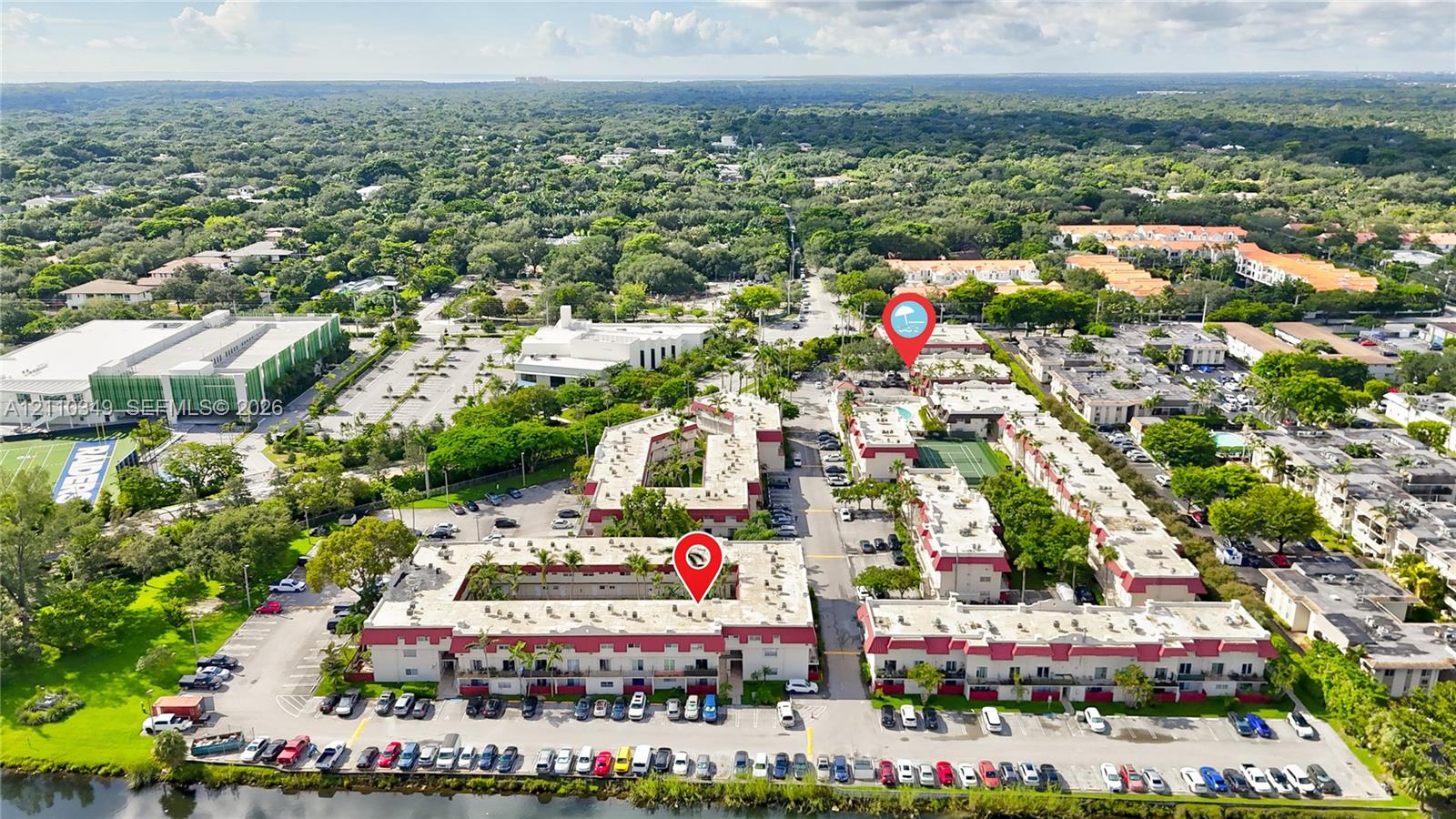 Aerial perspective of a multi-building residential complex featuring low-rise structures with red-tiled rooflines, shared courtyards, an outdoor swimming pool, and dedicated parking areas