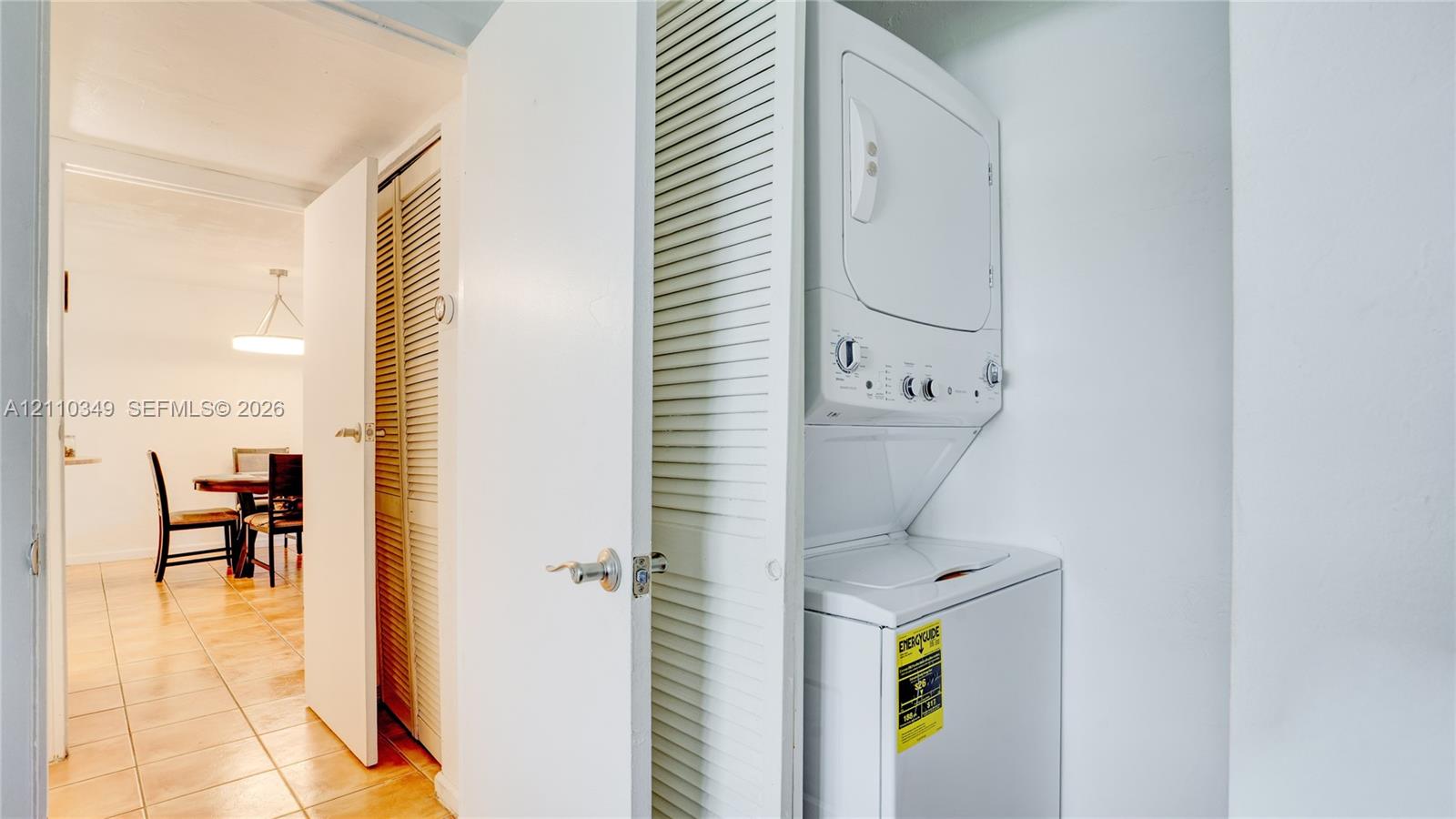 Stackable laundry unit housed within a closet featuring white louvered doors