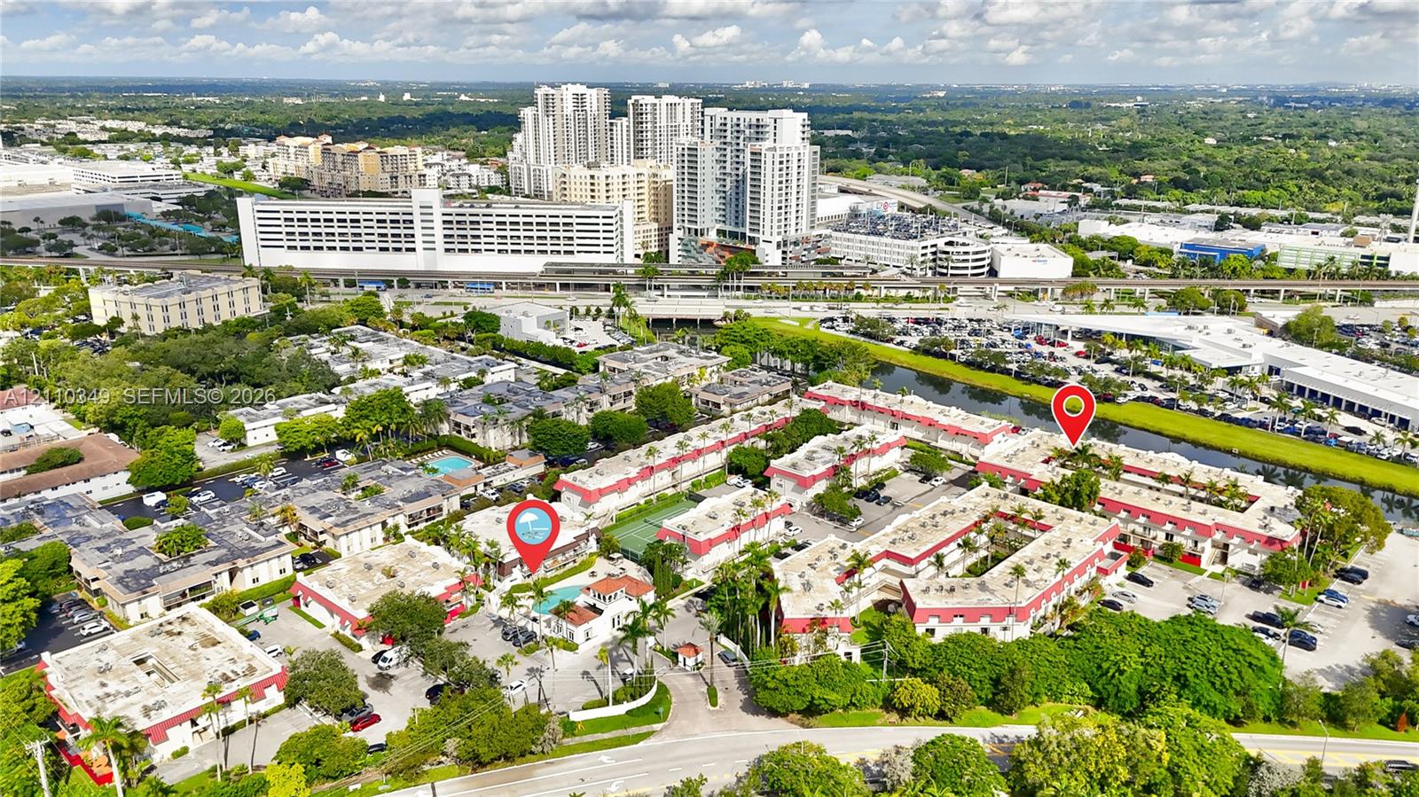 Aerial perspective of a multi-unit residential community featuring a centrally located swimming pool, tennis court, and dense perimeter landscaping