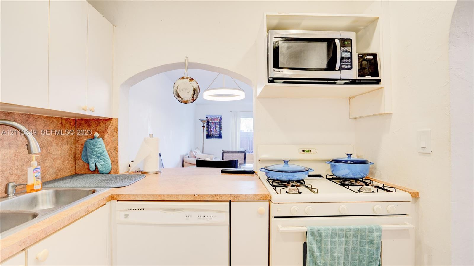 Kitchen featuring white cabinetry, an integrated gas range with overhead microwave, a stainless steel sink with a pull-down faucet, and an arched entryway