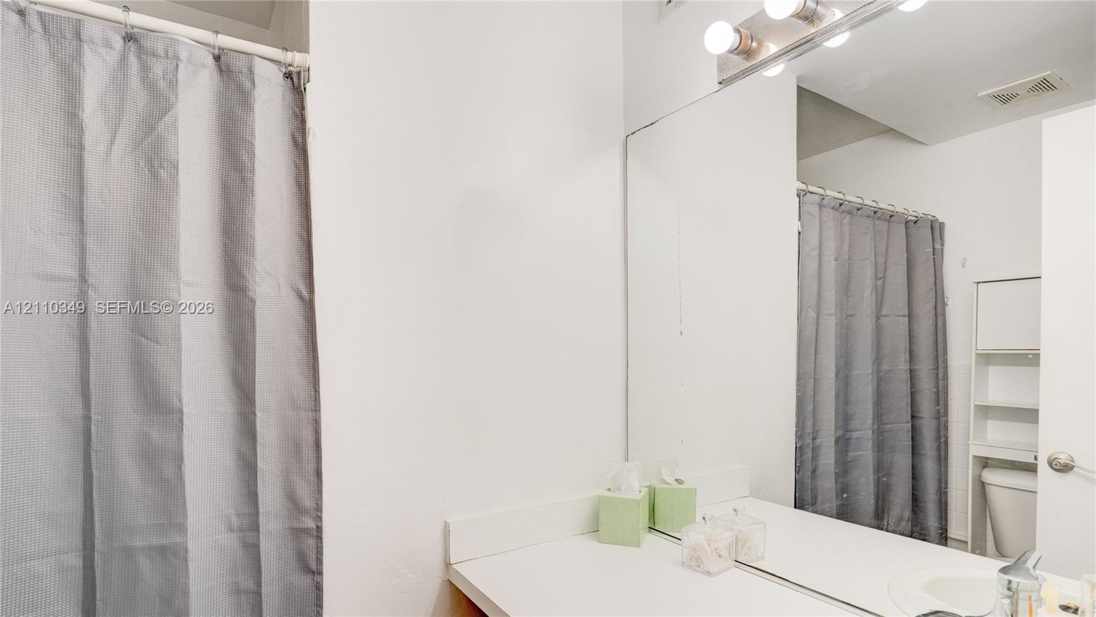 Bathroom featuring a full-width vanity mirror, a four-bulb vanity light fixture, and a built-in over-the-toilet storage unit