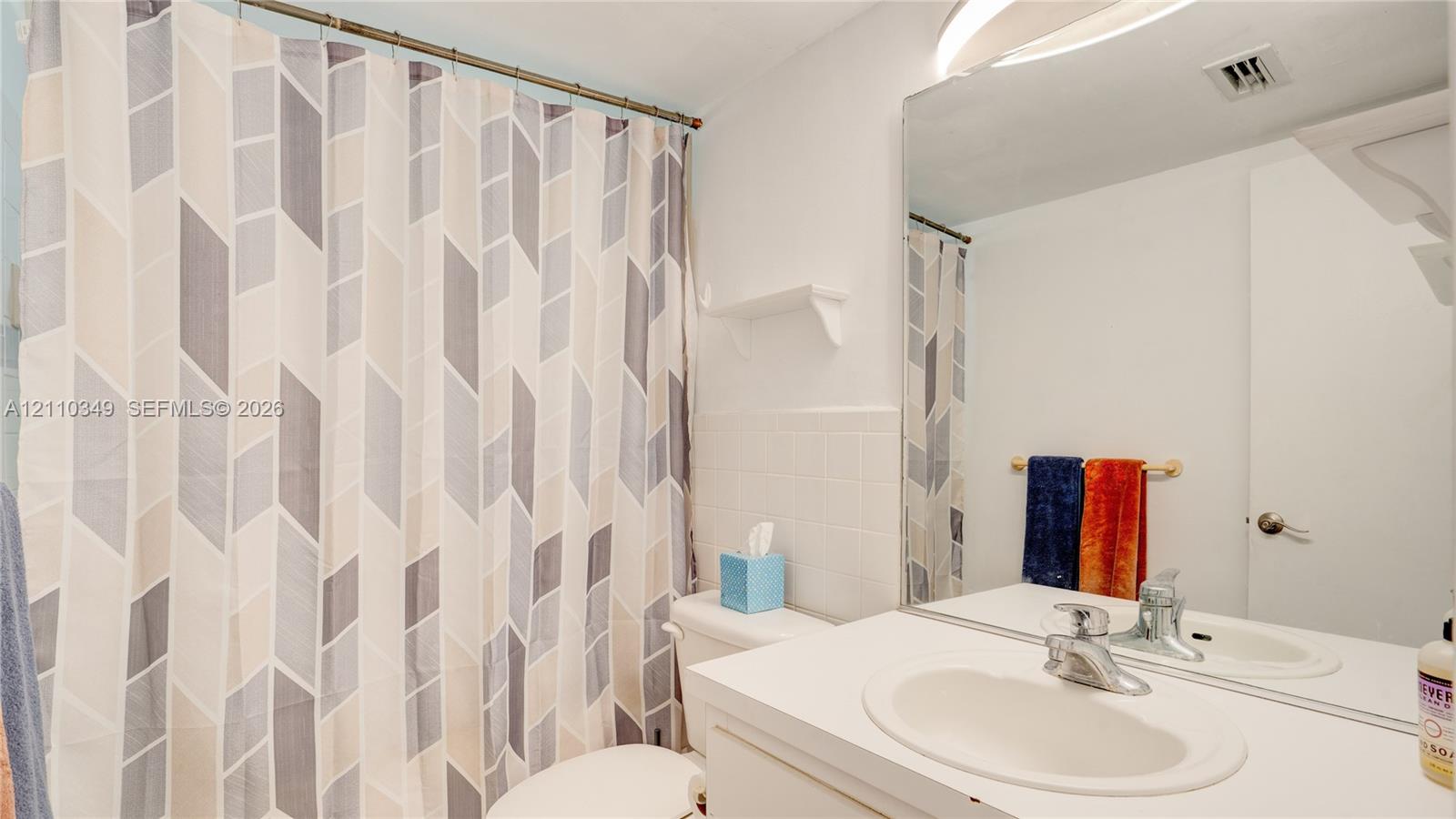 Bathroom featuring a white vanity with an integrated sink, polished chrome faucet, wall-spanning mirror, and white tile tub surround
