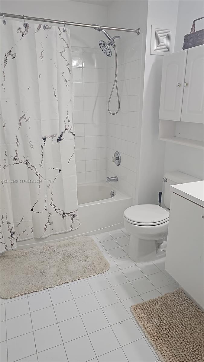 Bathroom featuring a white tile floor, a shower-tub combination with white surround tiling, a chrome handheld shower head, a white vanity cabinet, and wall-mounted storage cabinetry