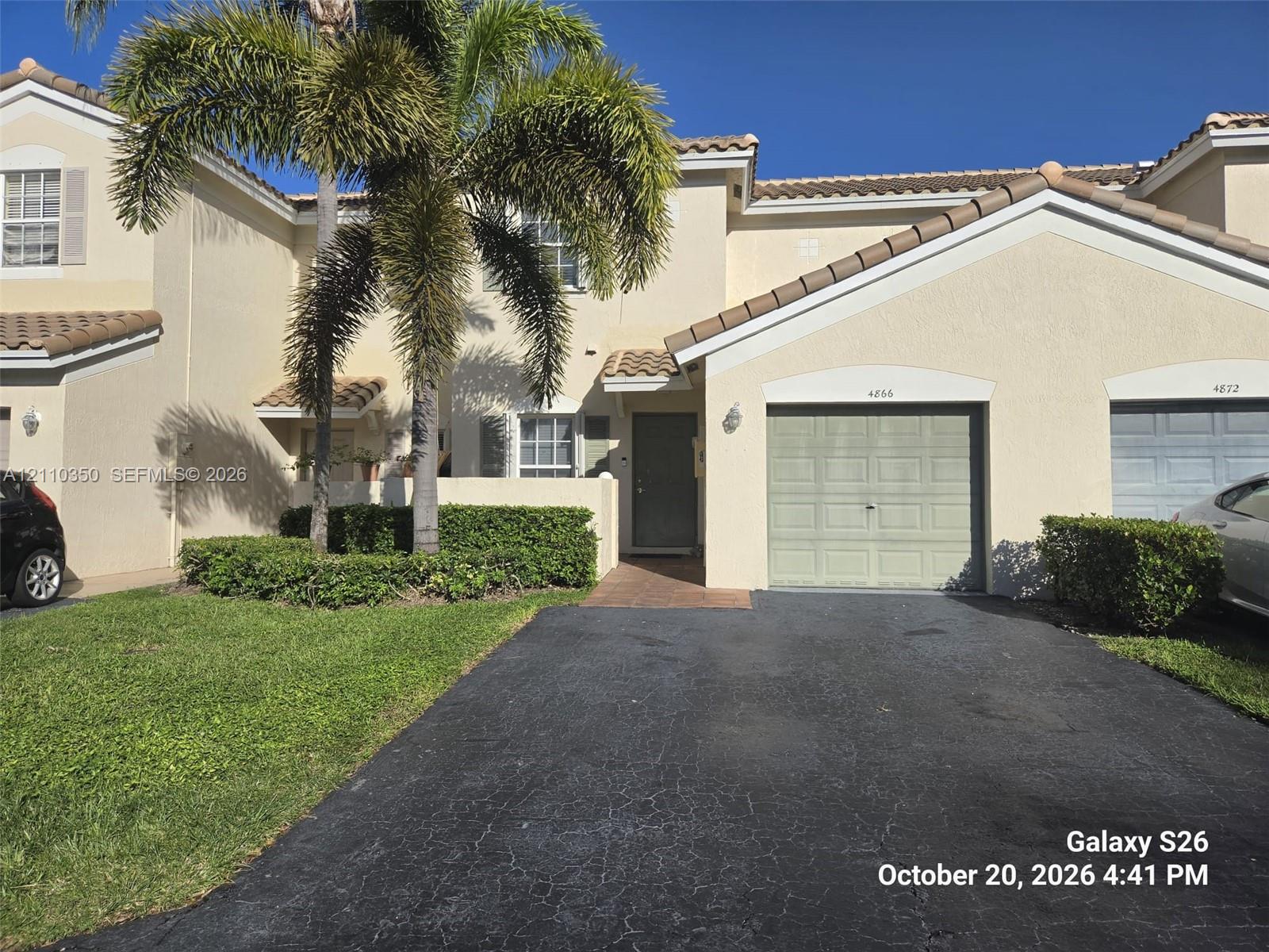 Stucco exterior featuring a tile roof, single-car garage with a paneled door, private entryway, and mature palm tree landscaping Stucco exterior featuring a tile roof, single-car garage with a paneled door, private entryway, and mature palm tree landscaping