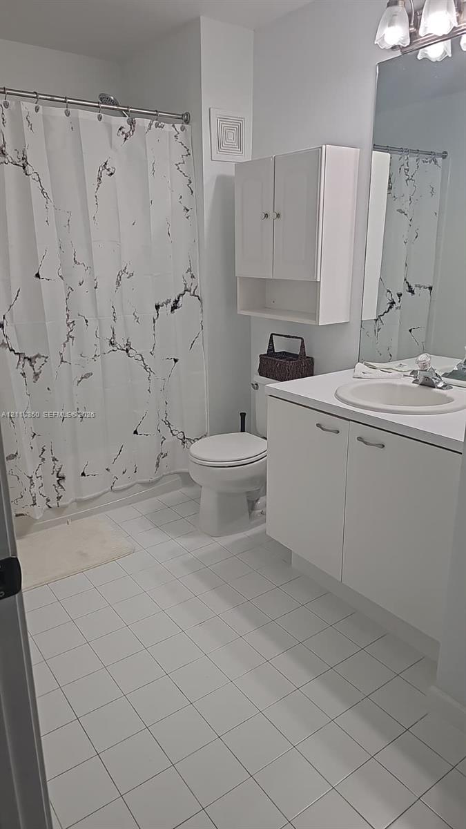 Bathroom featuring white tile flooring, white vanity cabinet with integrated sink, wall-mounted storage cabinetry, and a full-width mirror
