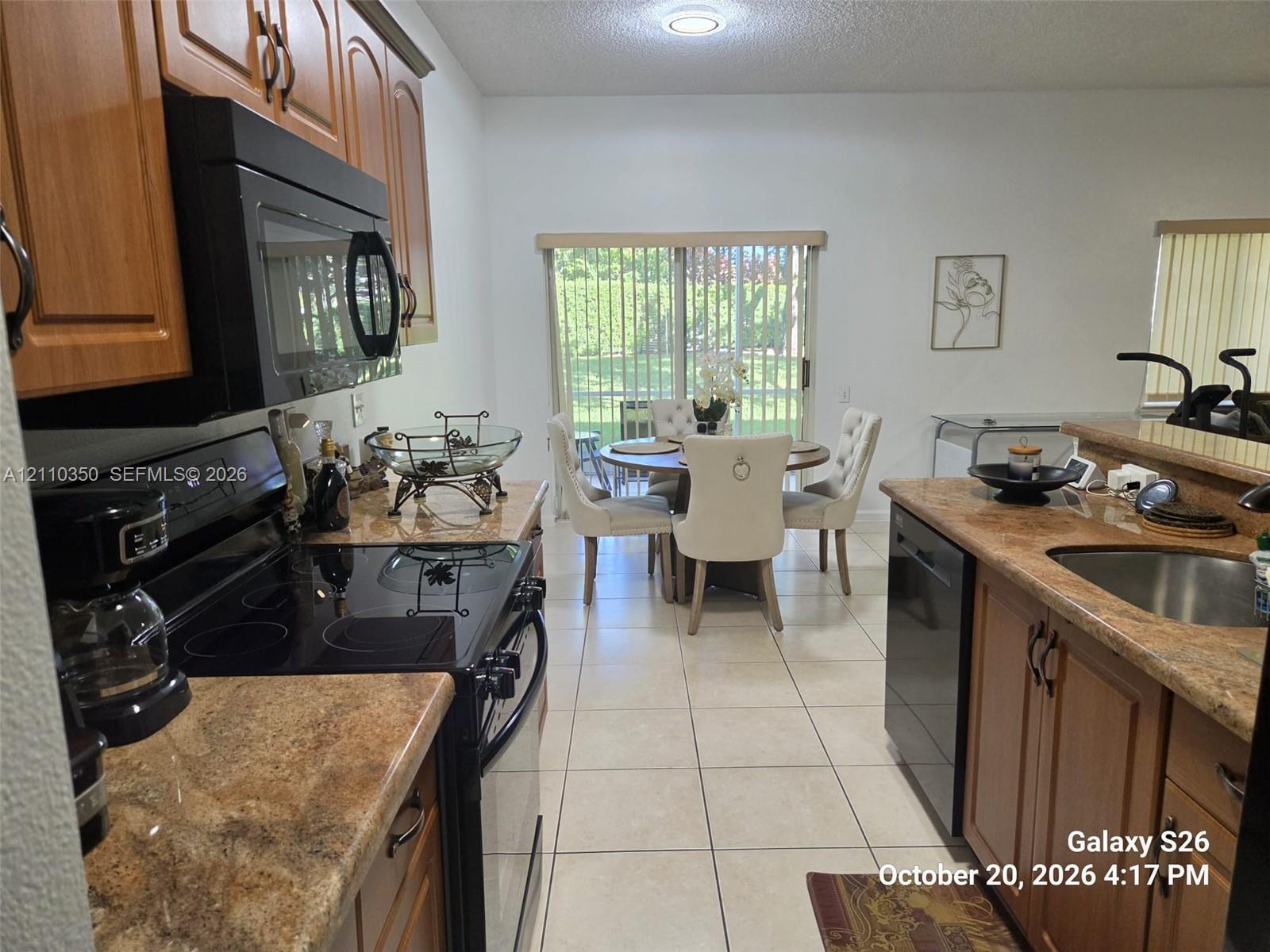 Kitchen featuring wood cabinetry, solid surface countertops, a black appliance suite, tile flooring, and a sliding glass door Kitchen featuring wood cabinetry, solid surface countertops, a black appliance suite, tile flooring, and a sliding glass door