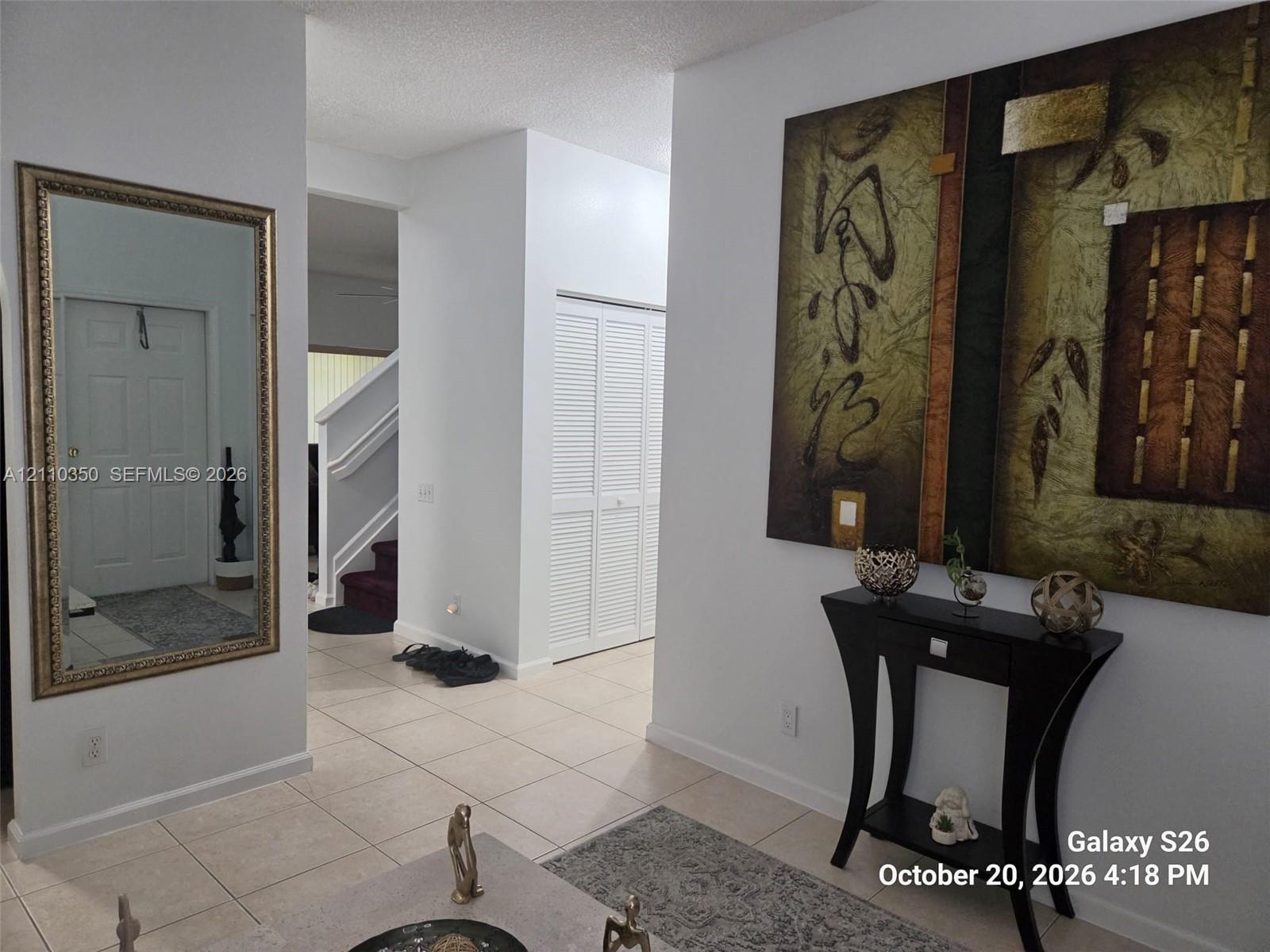 Foyer featuring neutral tile flooring, white wall-mounted louvered closet doors, and a wall-mounted decorative mirror Foyer featuring neutral tile flooring, white wall-mounted louvered closet doors, and a wall-mounted decorative mirror