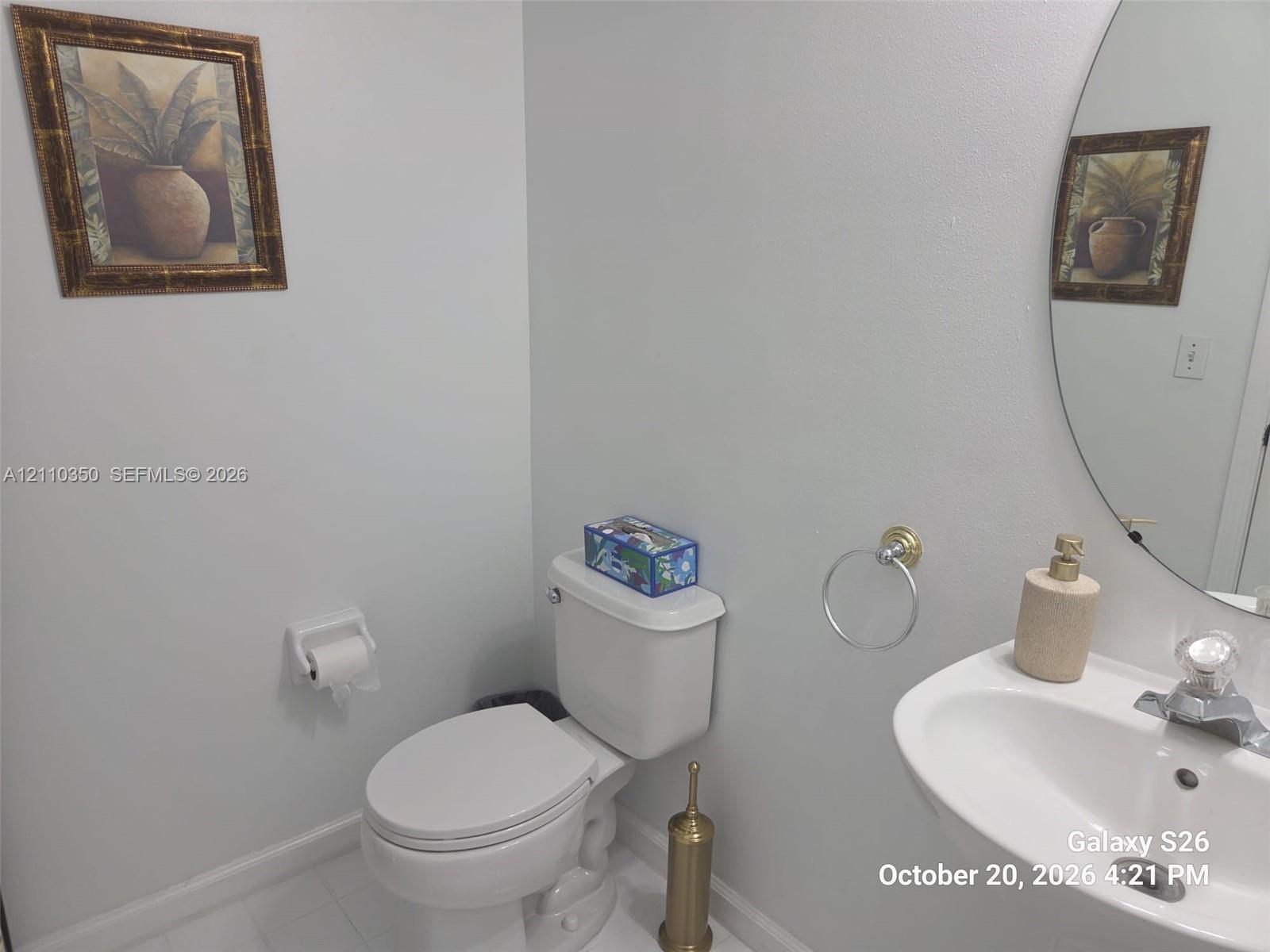Wall-mounted oval mirror, pedestal sink with chrome-finish faucet, and rounded bowl toilet