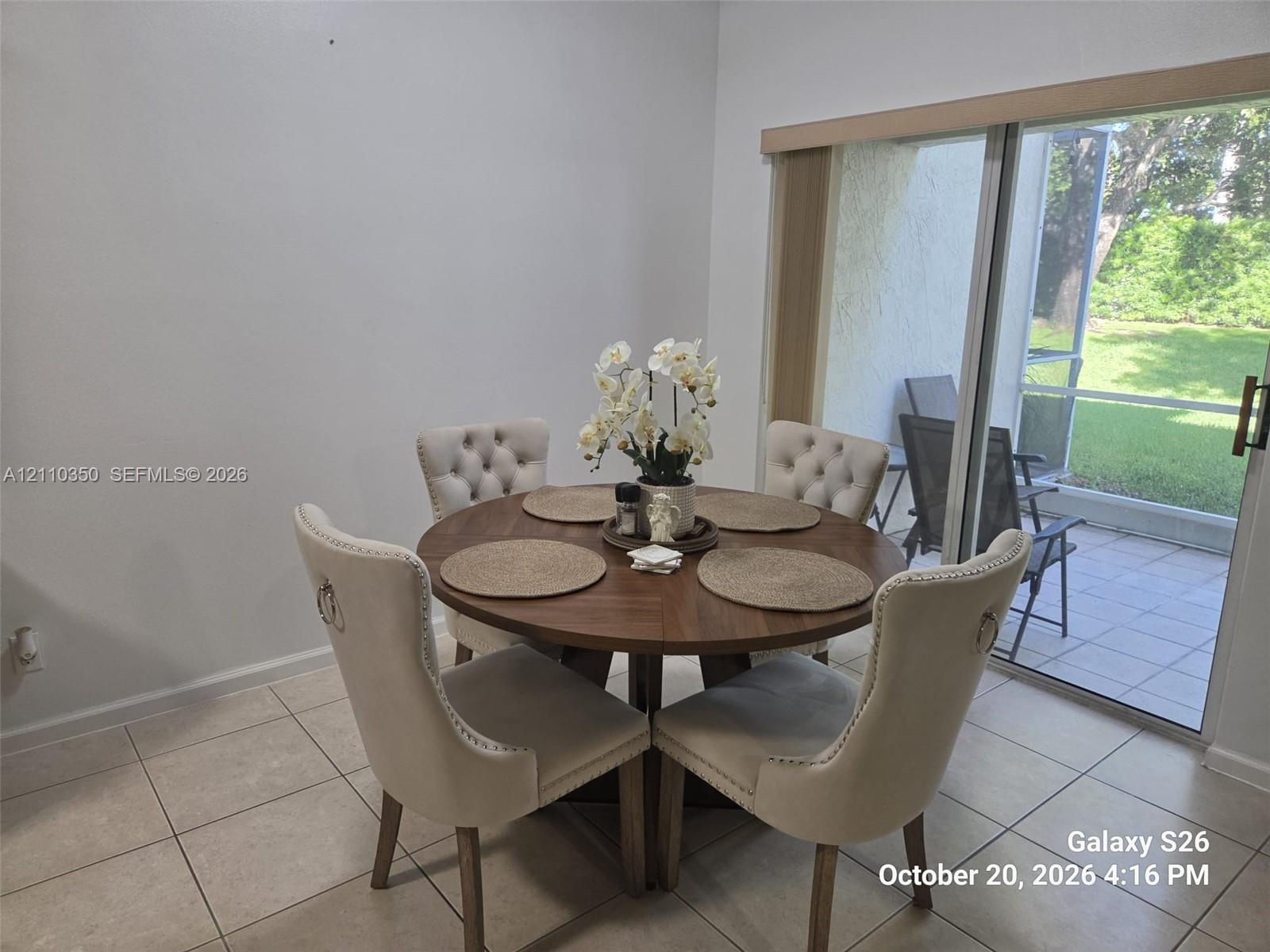 Neutral tile flooring and oversized sliding glass door leading to a screened lanai with a concrete patio
