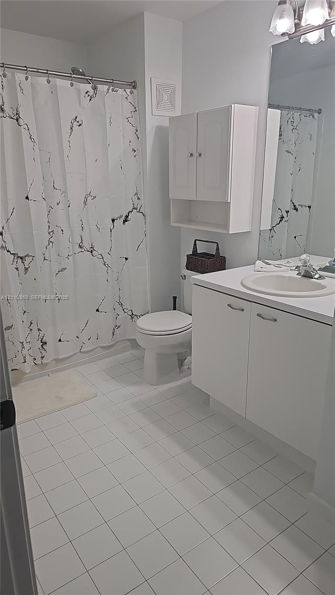 Bathroom featuring white ceramic tile flooring, vanity with an integrated basin, wall-mounted storage cabinetry, and a full-length mirror