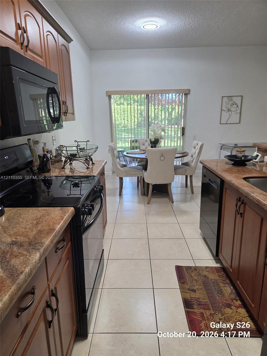 Kitchen featuring wood-finish cabinetry, stone-finish countertops, black built-in appliances, ceramic tile flooring, and a sliding glass door Kitchen featuring wood-finish cabinetry, stone-finish countertops, black built-in appliances, ceramic tile flooring, and a sliding glass door