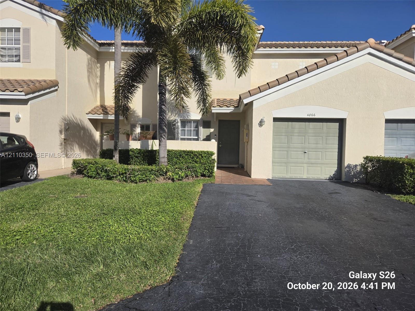 Stucco exterior featuring a tiled roof, attached single-car garage, paved driveway, and mature landscaping Stucco exterior featuring a tiled roof, attached single-car garage, paved driveway, and mature landscaping
