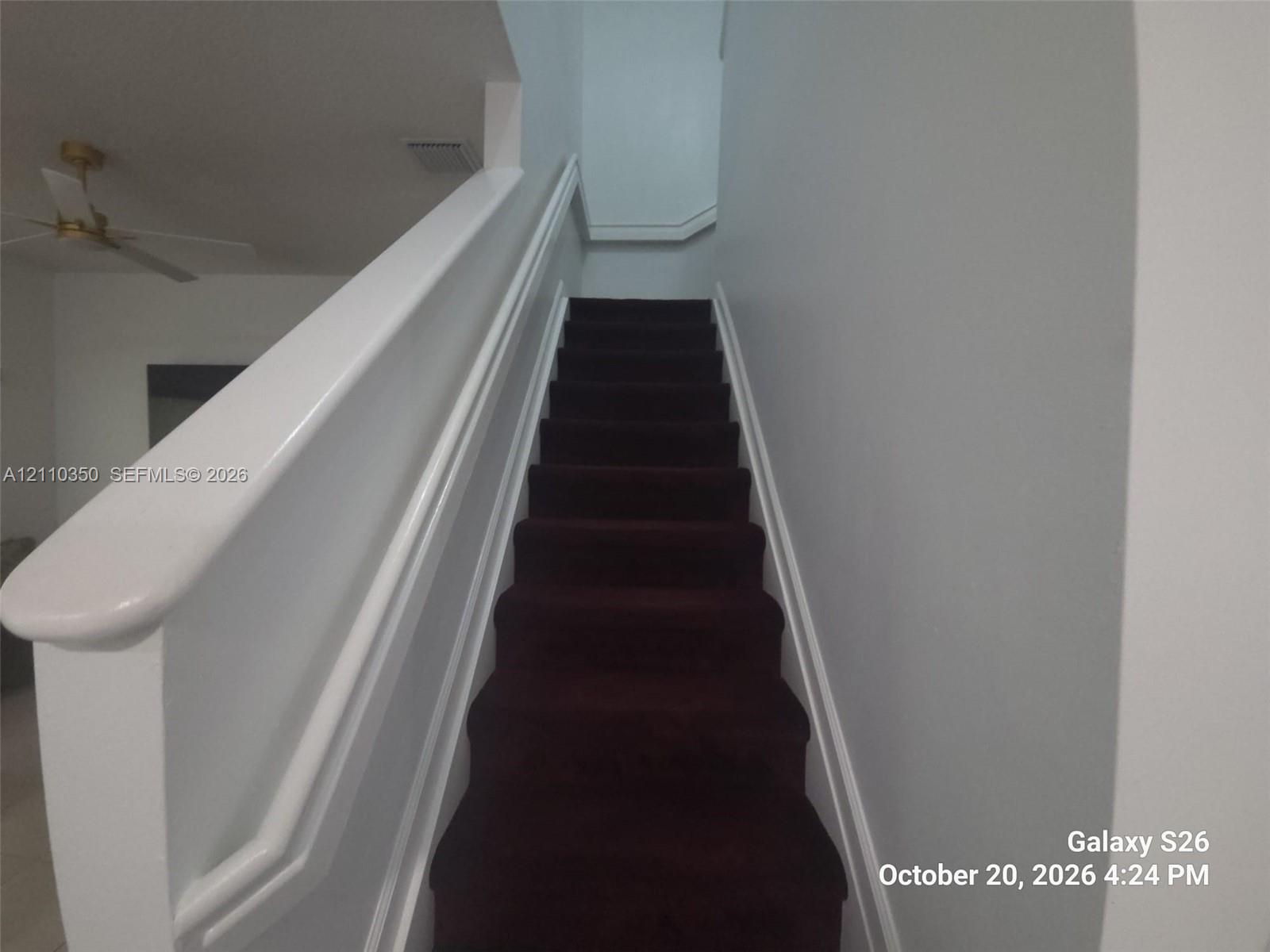 Staircase featuring dark carpeted treads and a white painted handrail with matching trim