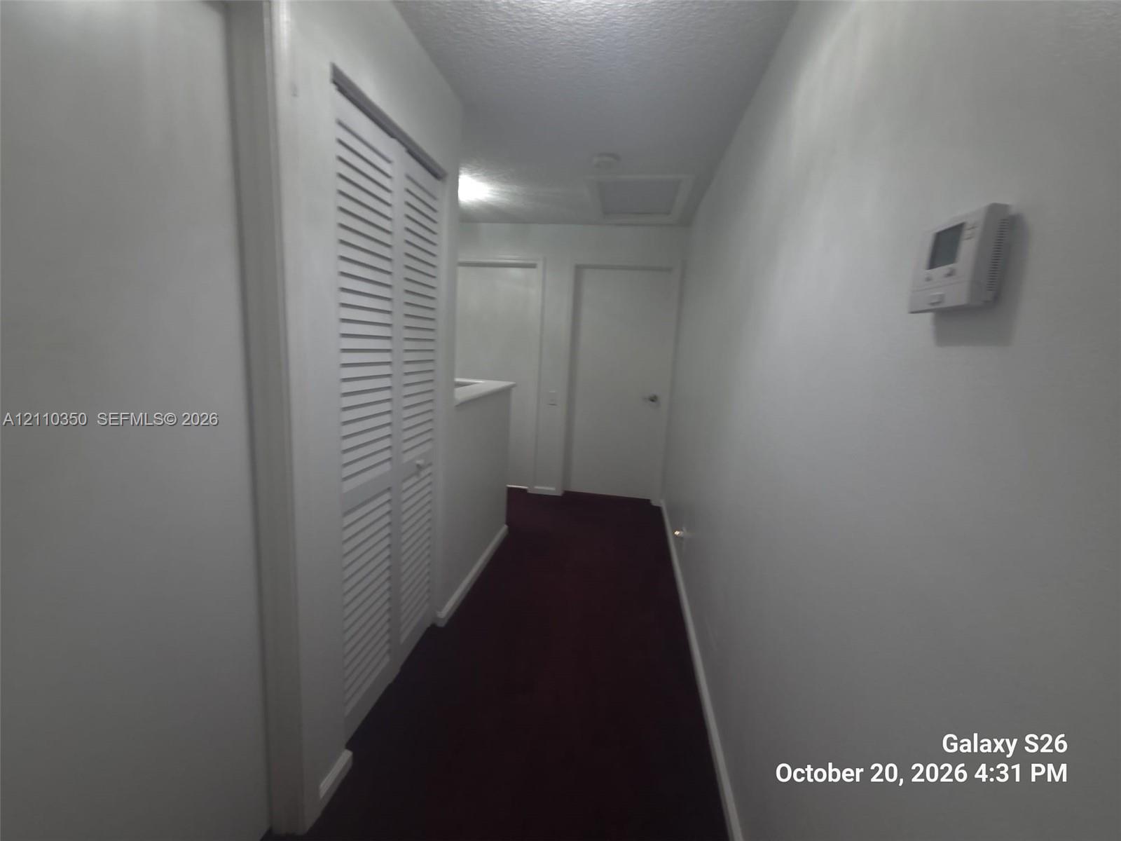 Interior hallway featuring louvered bi-fold closet doors, wall-mounted thermostat, and solid-core interior doors