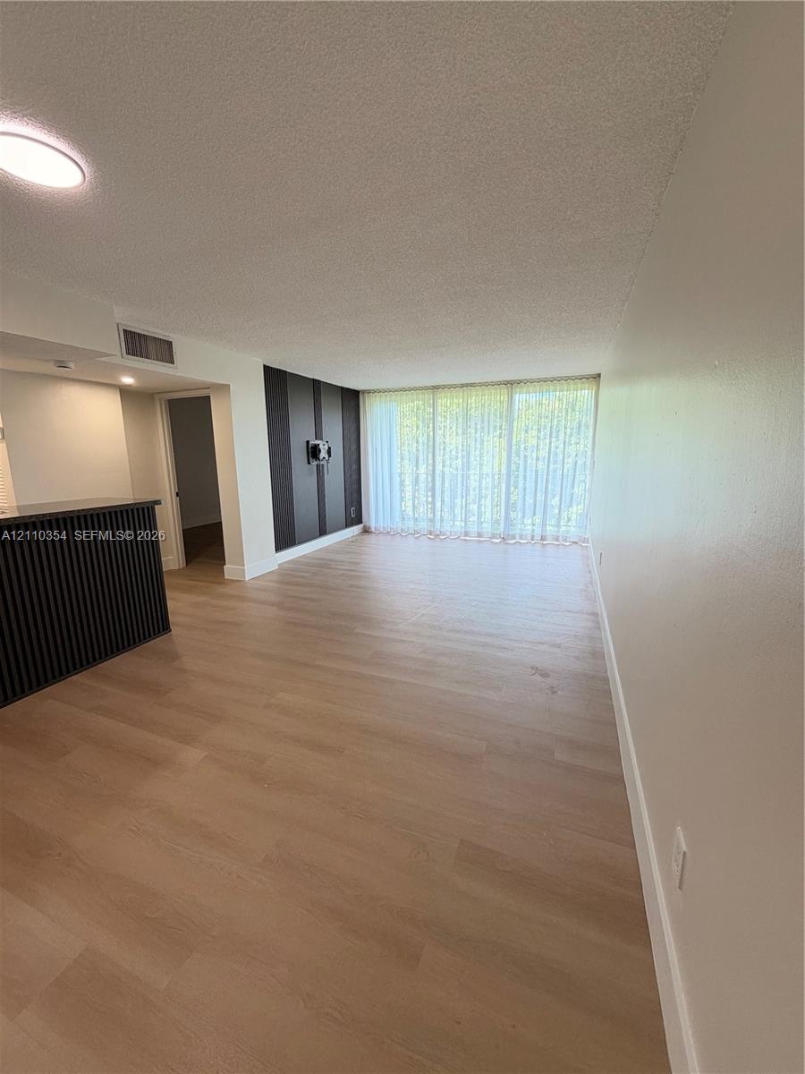 Open-concept living space featuring wood-finish flooring, floor-to-ceiling glass wall, accent wall with vertical paneling, and a kitchen peninsula with integrated vertical slat detailing