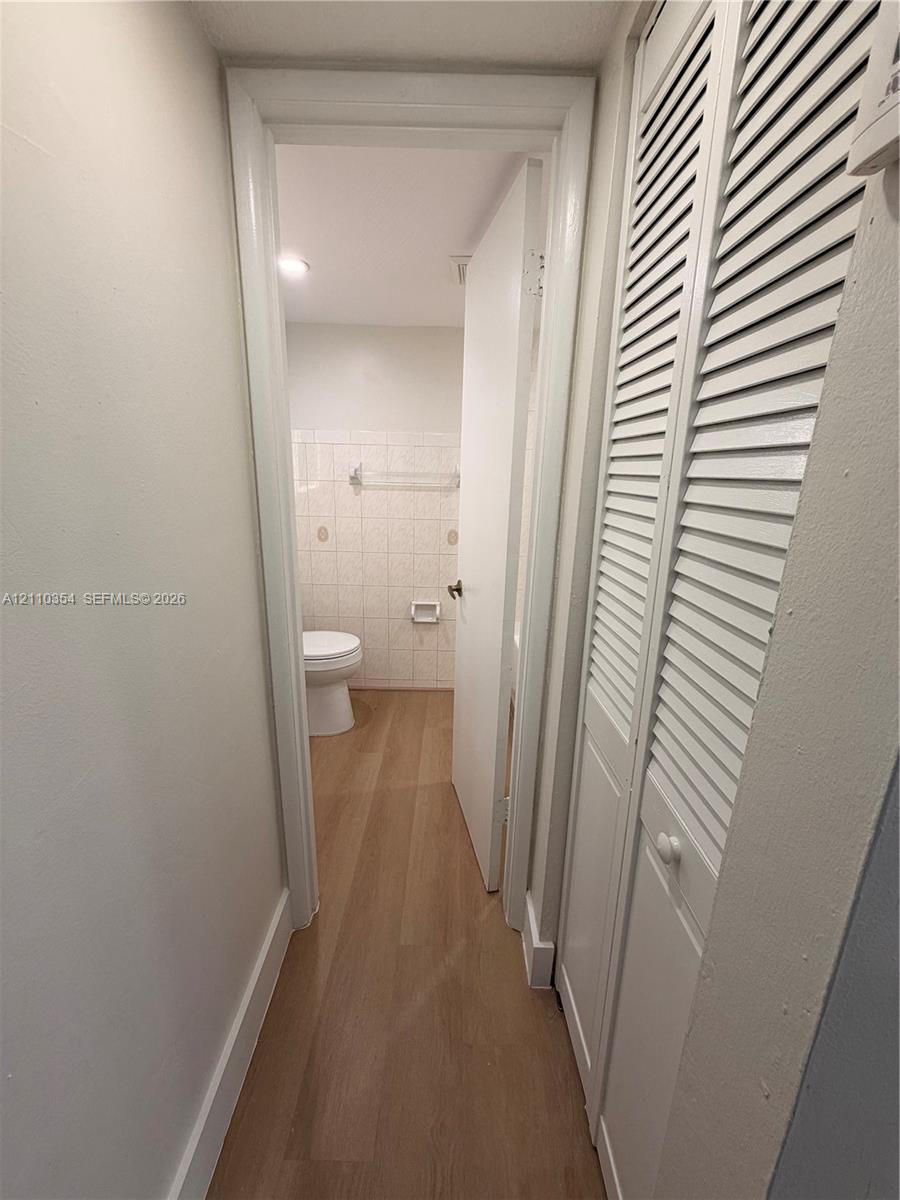 Hallway featuring wood-finish flooring and white louvered-door closets, leading to a space with tile-surround walls