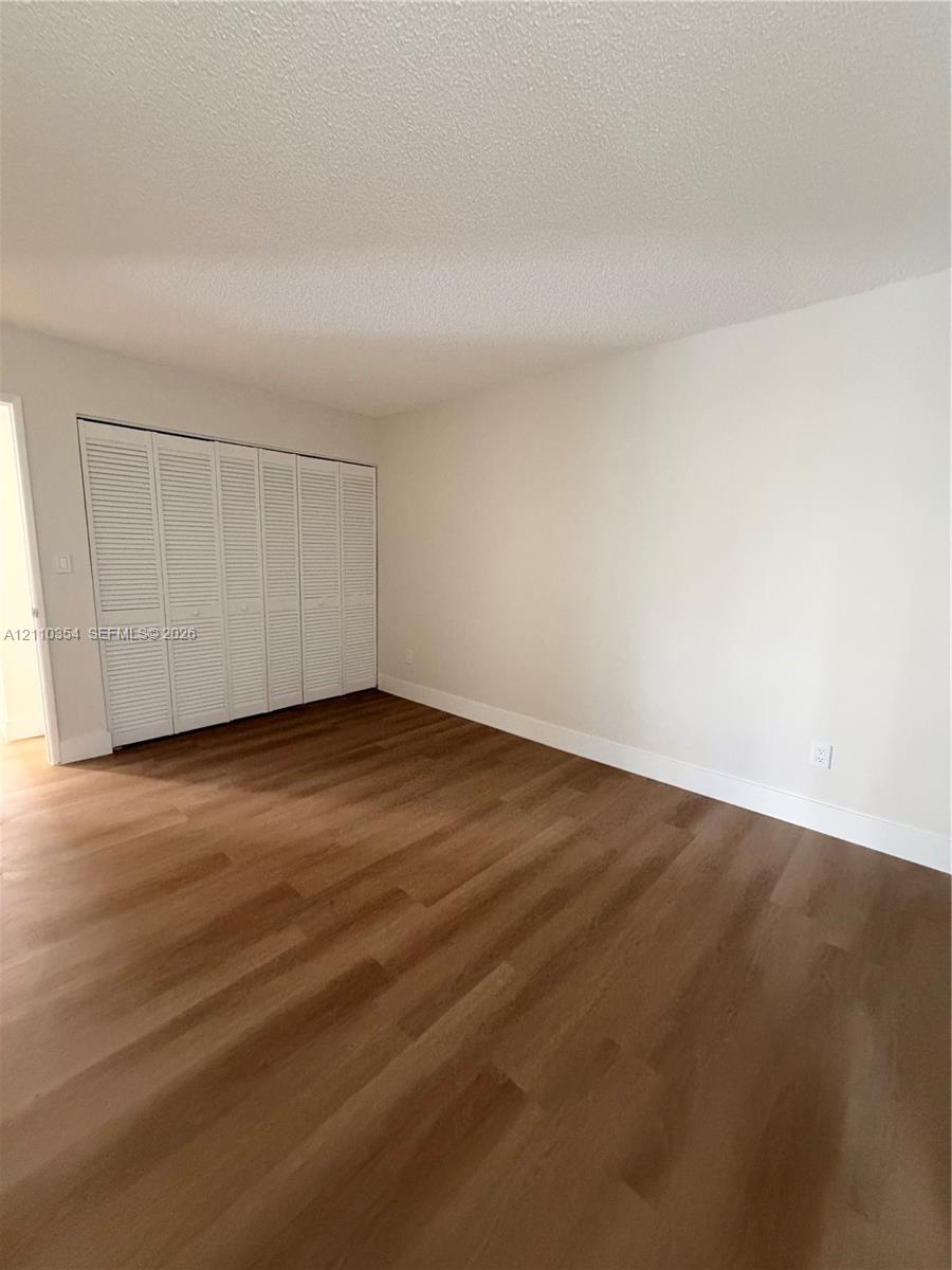 Room featuring wood-finish flooring, neutral walls, and a large reach-in closet with white louvered bi-fold doors