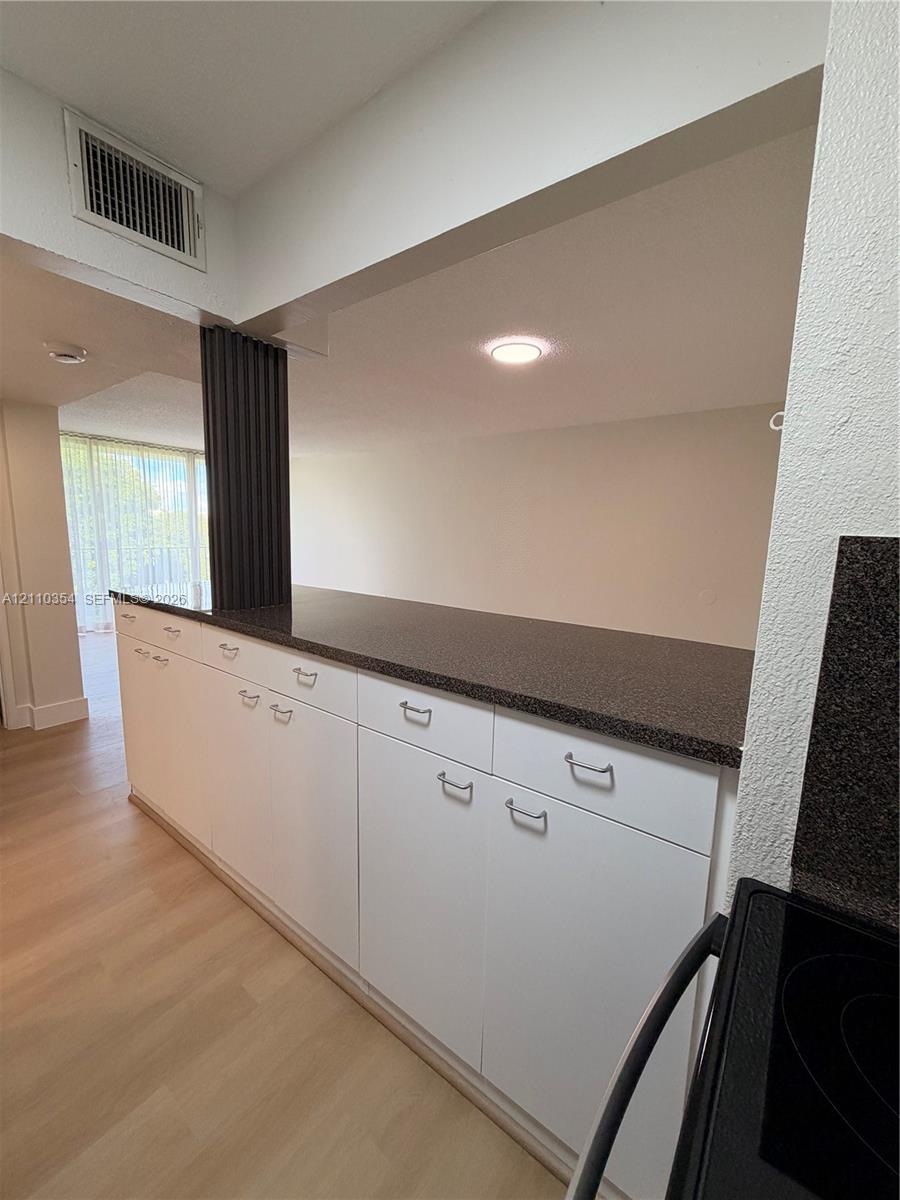 Kitchen pass-through featuring a dark stone-finish countertop, white cabinetry with silver-tone hardware, and wood-finish flooring