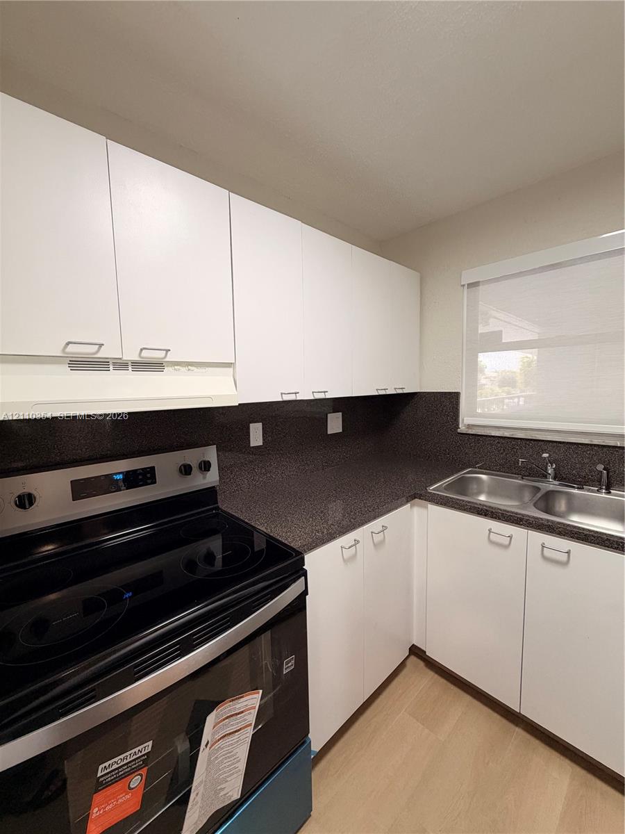 Kitchen featuring white flat-panel cabinetry, dark stone-finish countertops, stainless steel dual-basin sink, and integrated electric range