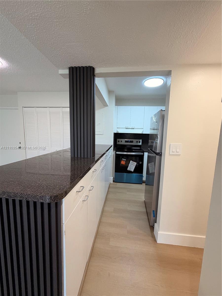 Kitchen featuring white cabinetry, dark stone-finish countertops, wood-finish flooring, and a decorative slatted support pillar