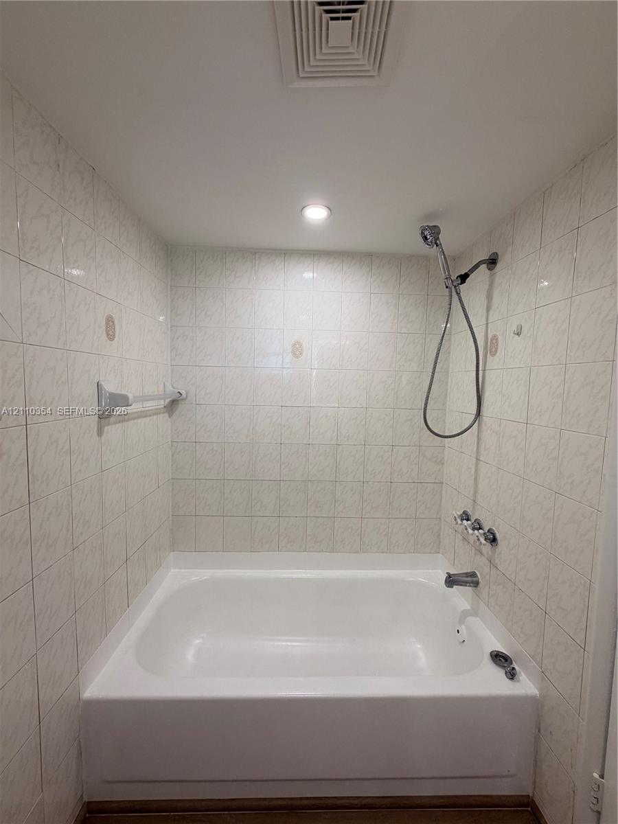 Alcove bathtub featuring white tile wall surround, chrome handheld shower fixture, integrated metal towel bar, and recessed lighting