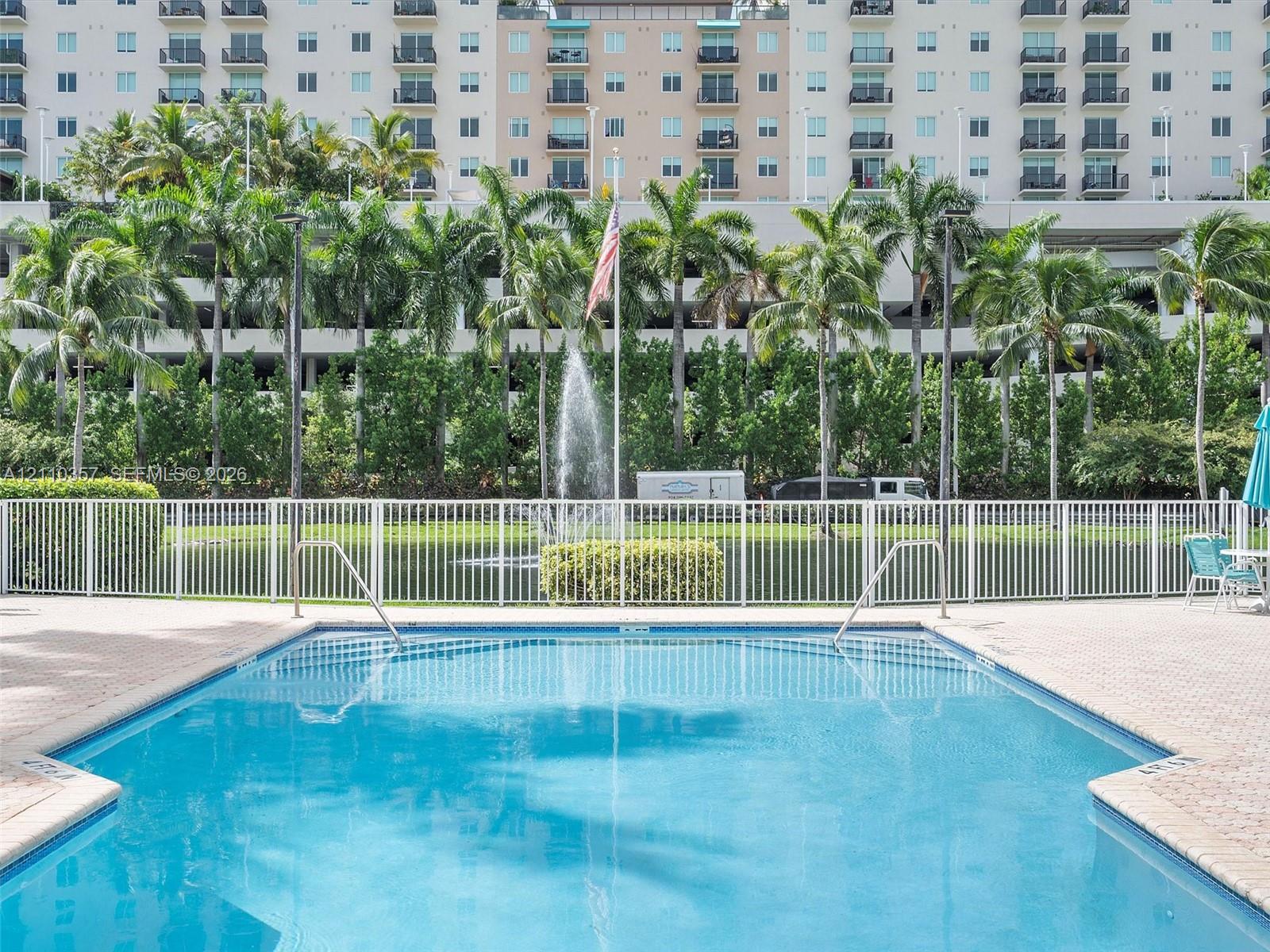 Swimming pool featuring a paver deck, white metal perimeter fencing, and a water fountain backdrop