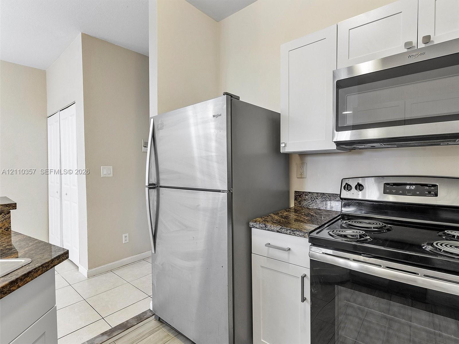 Kitchen featuring white shaker-style cabinetry, stone-finish countertops, stainless steel refrigerator, built-in microwave, and tile flooring