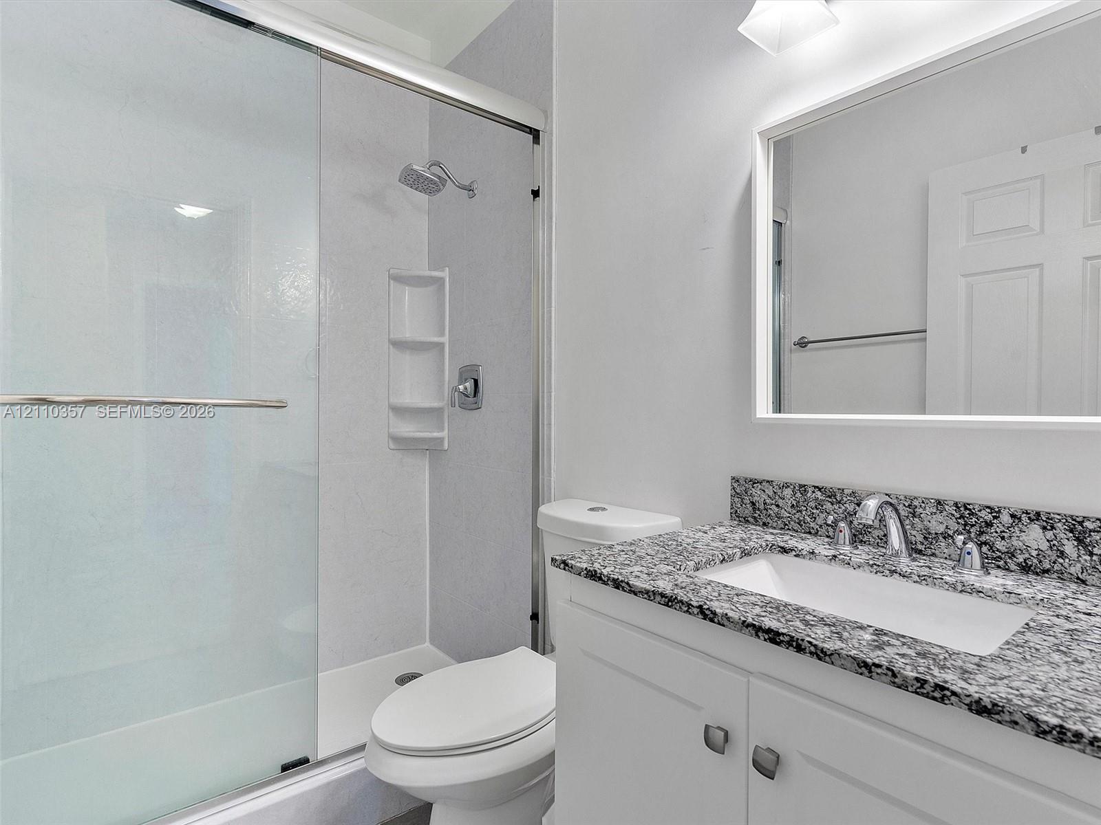 Bathroom featuring a vanity with a stone-finish countertop, undermount sink, framed mirror, and a walk-in shower with a glass enclosure and integrated shelving
