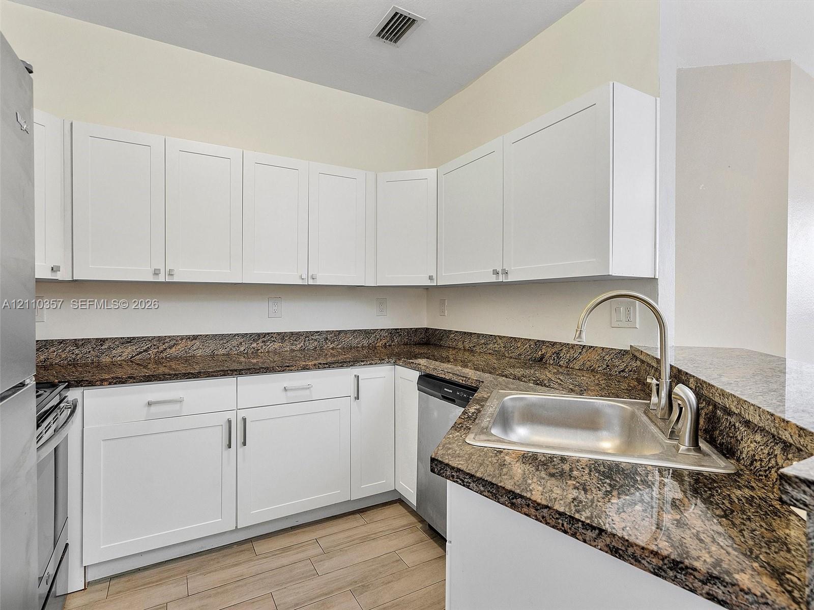 Kitchen featuring white shaker-style cabinetry, stone-finish countertops, stainless steel appliances, stainless steel undermount sink with arched faucet, and wood-finish tile flooring