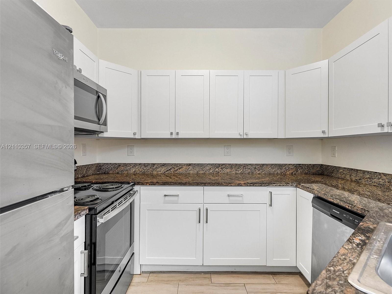 Kitchen featuring white Shaker-style cabinetry, dark stone countertops, stainless steel appliances, and wood-finish flooring