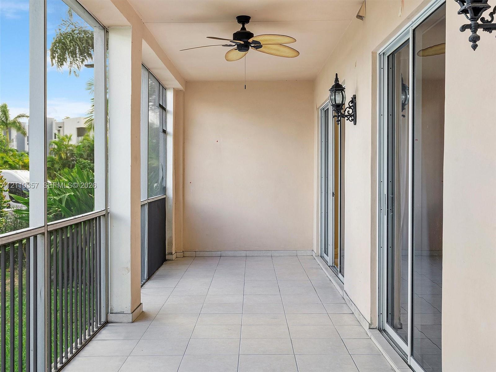Screened-in patio featuring tiled flooring, a ceiling fan, dual sliding glass door access, and wall-mounted carriage-style light fixtures