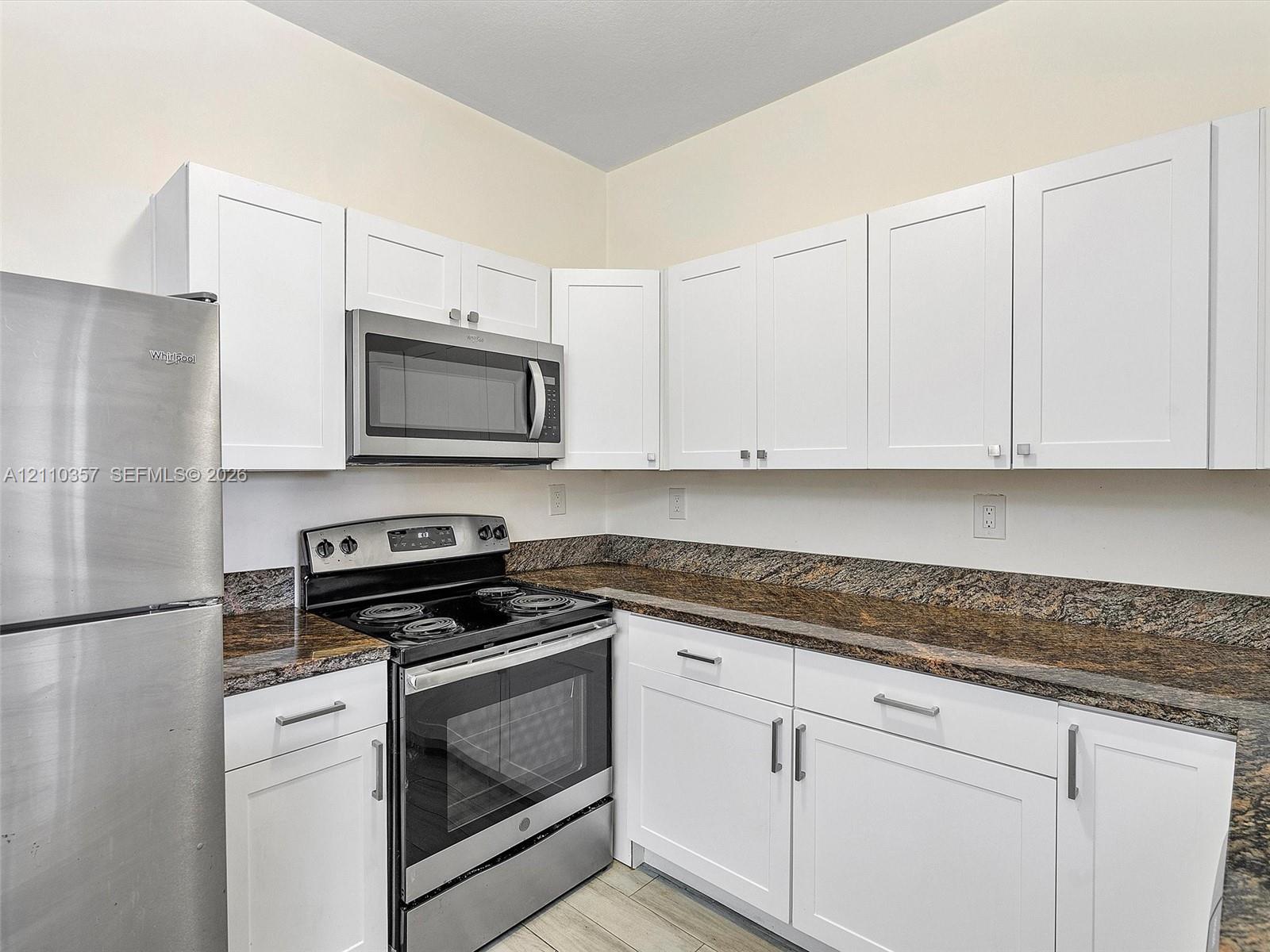 Kitchen featuring white shaker-style cabinetry, stone countertops, integrated stainless steel appliances, and wood-finish flooring