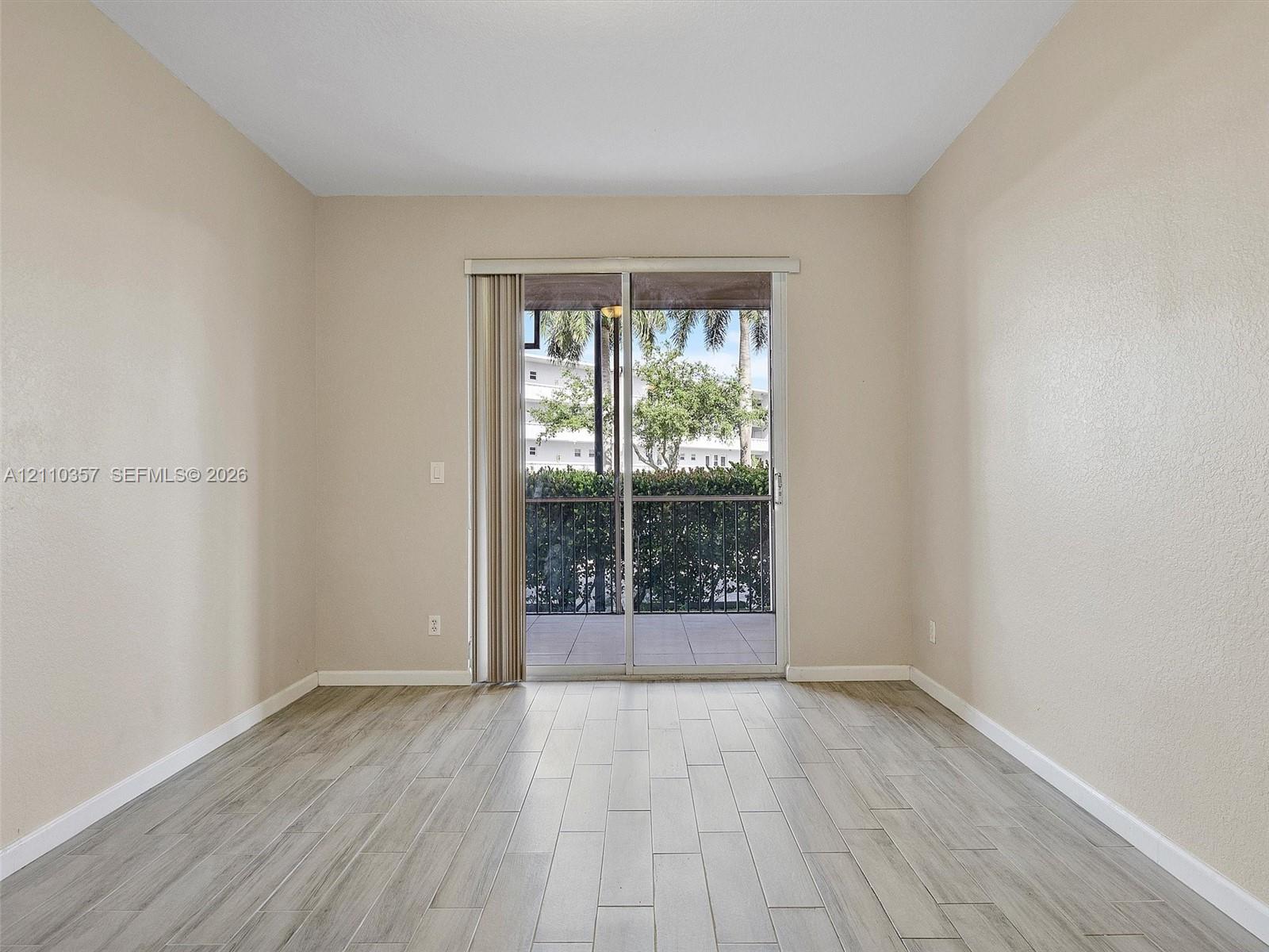 Interior room featuring neutral wall paint, wood-finish flooring, and sliding glass doors with vertical blinds opening to a covered balcony