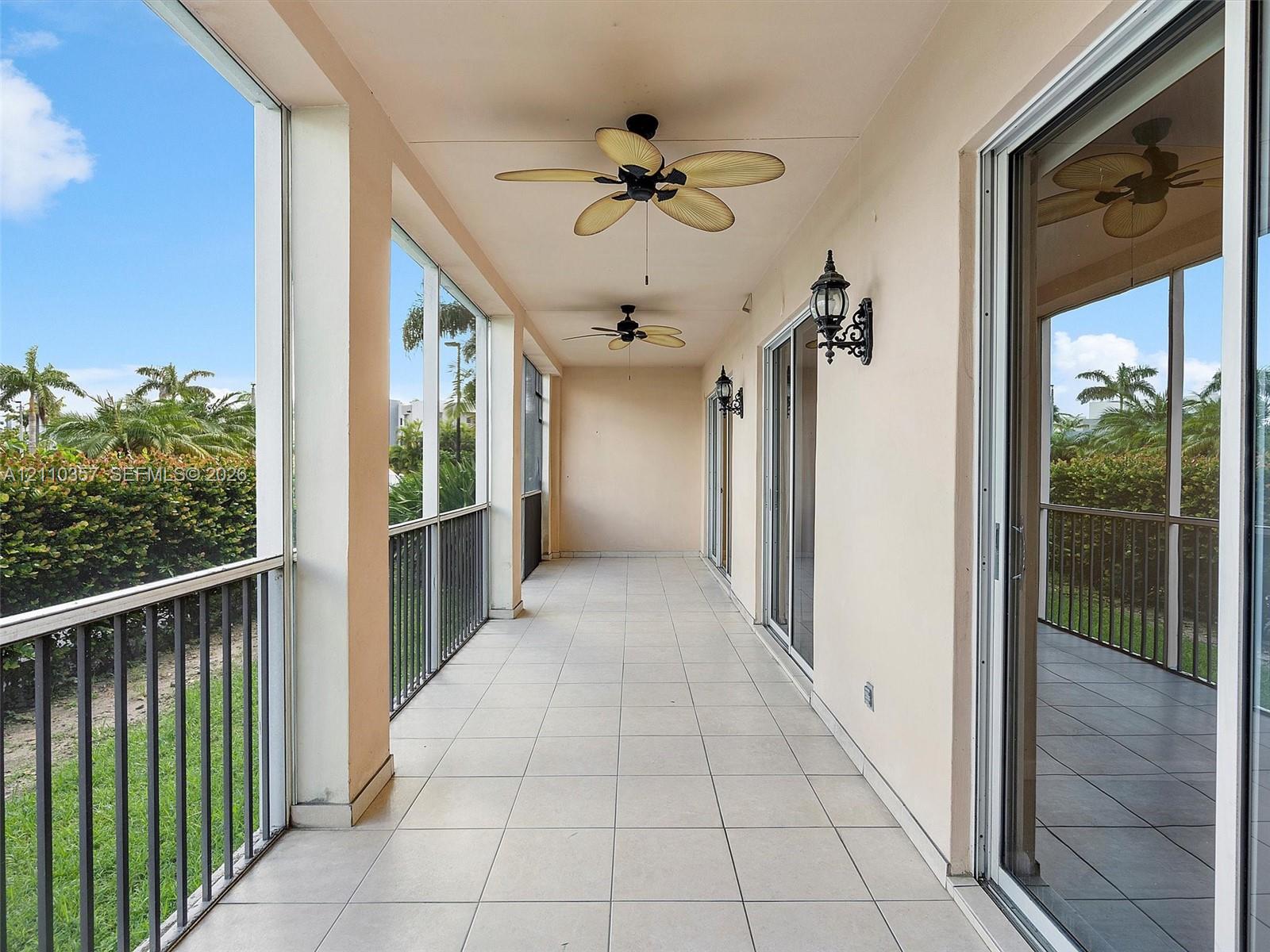 Screened-in covered porch featuring ceramic tile flooring, ceiling fans, wall-mounted coach lighting, and metal railings overlooking green space
