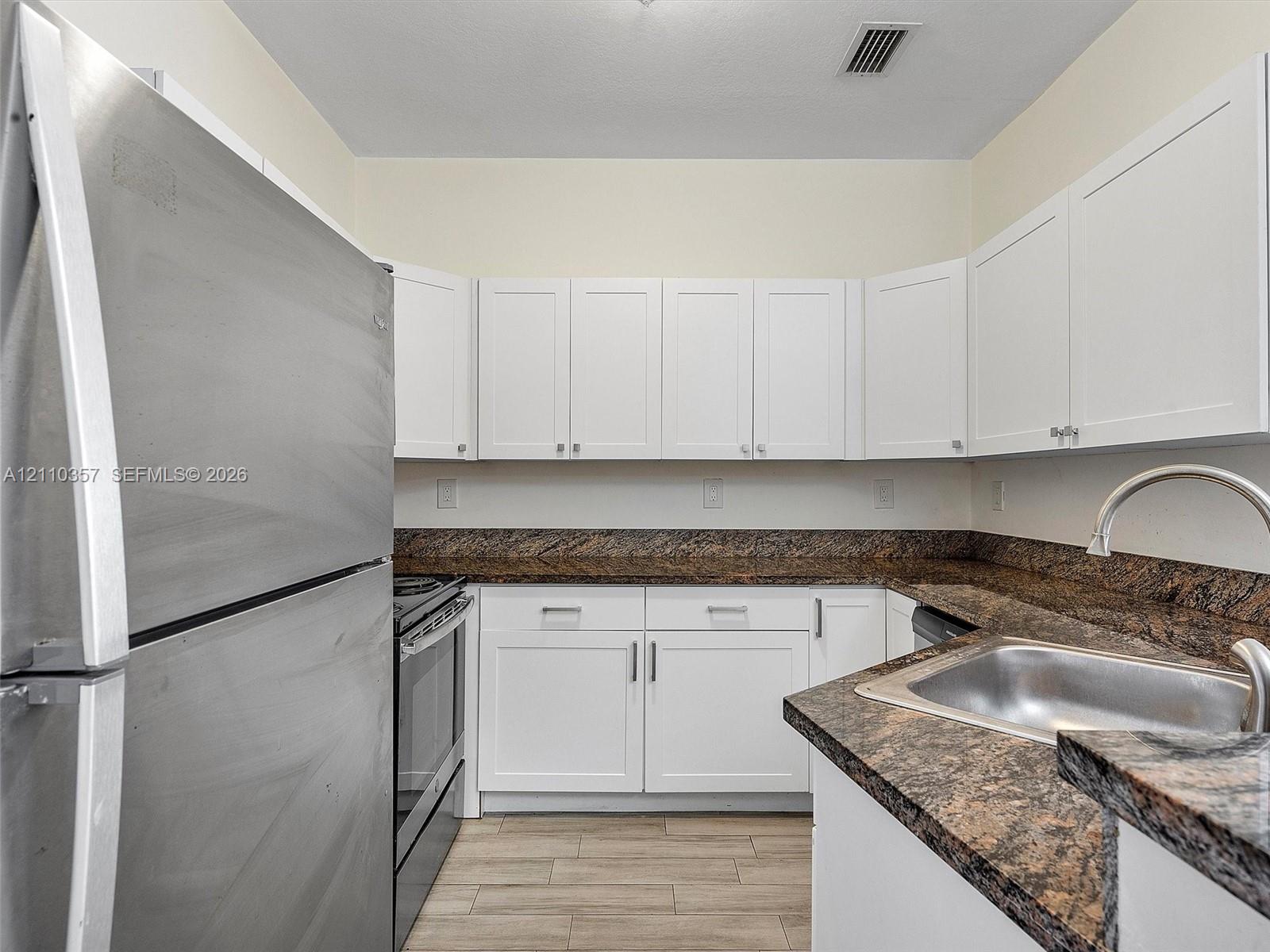 Kitchen featuring white shaker-style cabinetry, stone-finish countertops, stainless steel refrigerator, stainless steel range, and wood-finish flooring