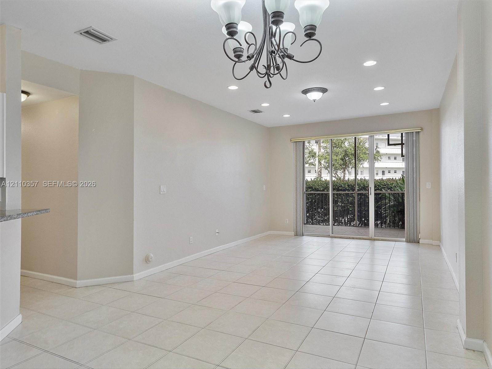 Neutral-toned interior featuring ceramic tile flooring, a decorative multi-arm chandelier, recessed ceiling lighting, and floor-to-ceiling sliding glass doors