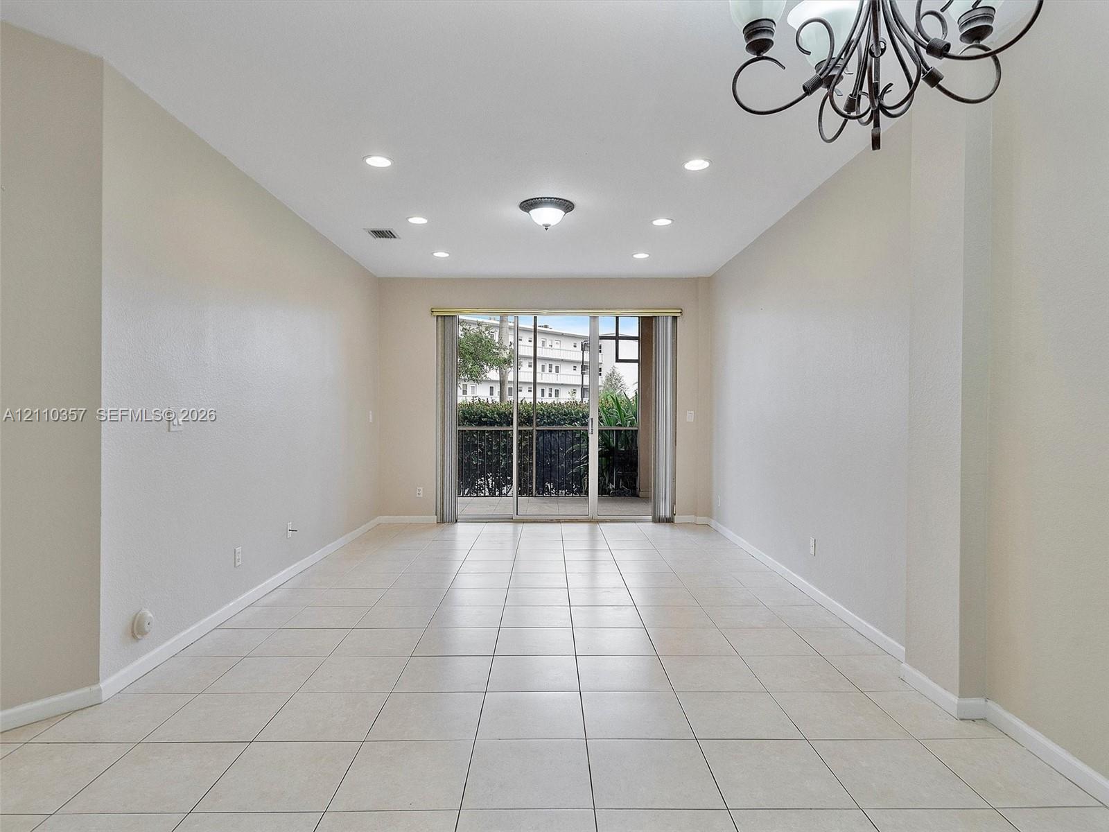 Neutral-toned room featuring tile flooring, recessed lighting, a decorative chandelier, and sliding glass doors with screen enclosure
