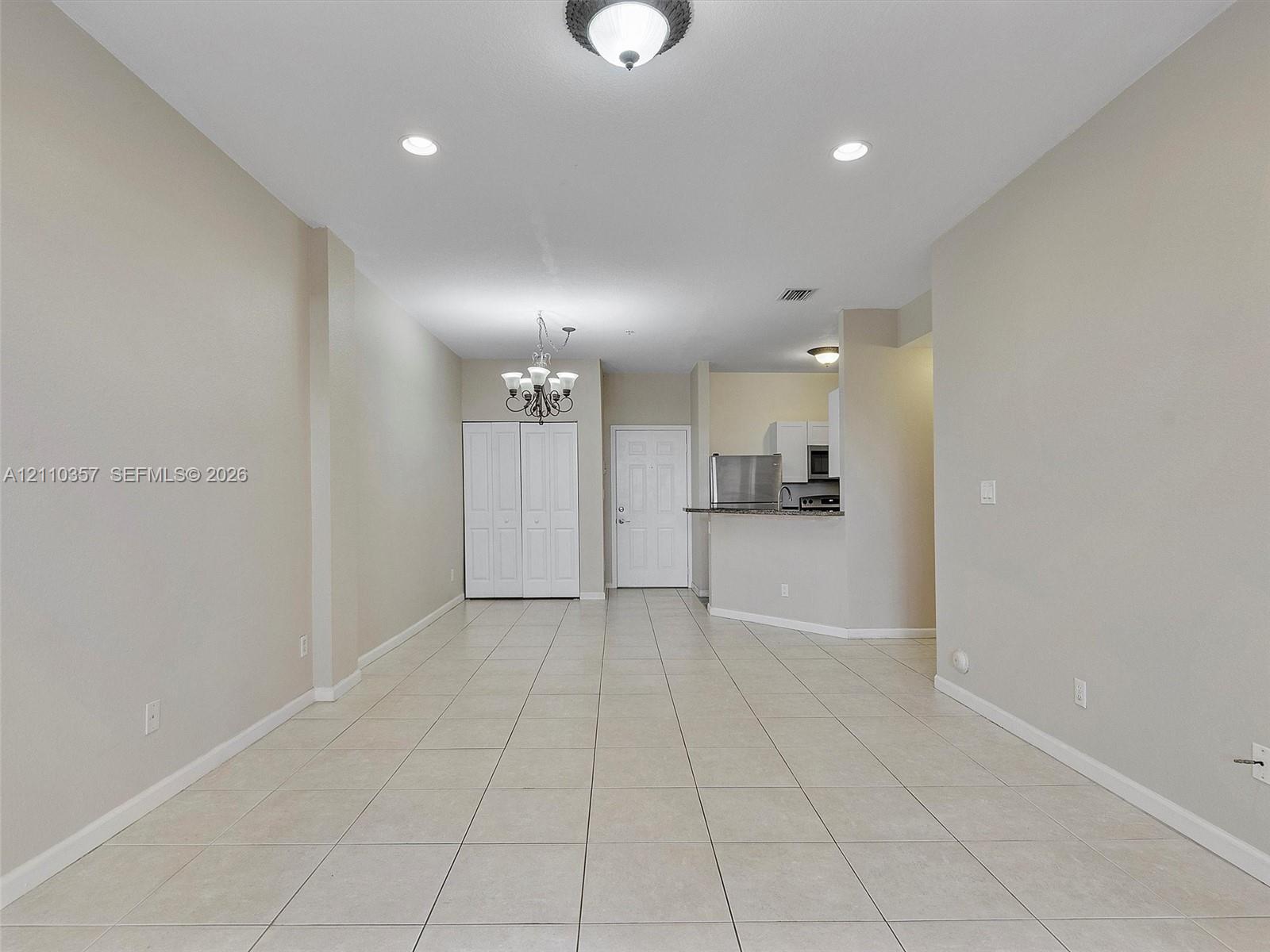 Open-concept interior featuring neutral wall tones, large-format tile flooring, recessed lighting, a decorative chandelier, and a breakfast bar with stone-finish countertops