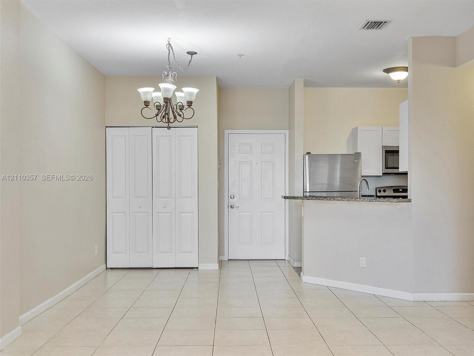 Neutral tile flooring, overhead chandelier, white closet doors, and kitchen area featuring a breakfast bar and stainless steel appliances
