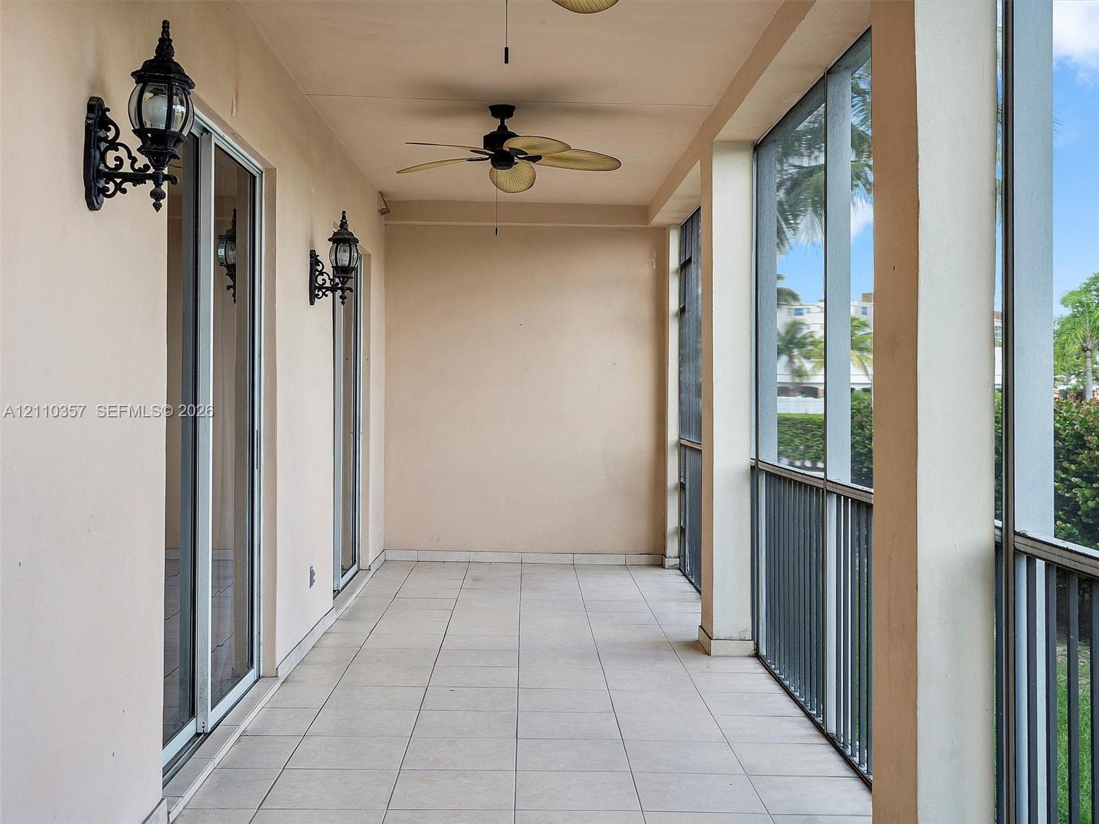 Screened-in porch featuring large-format tile flooring, double glass sliding doors, dark metal wall-mounted exterior light fixtures, and a ceiling-mounted fan