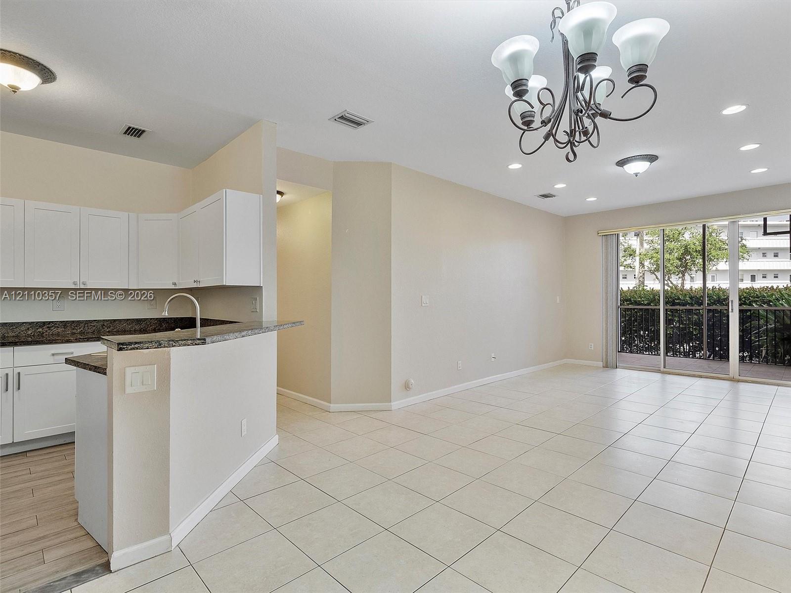 Open-concept kitchen featuring white cabinetry, stone-finish countertops, tile flooring, a decorative chandelier, and sliding glass doors